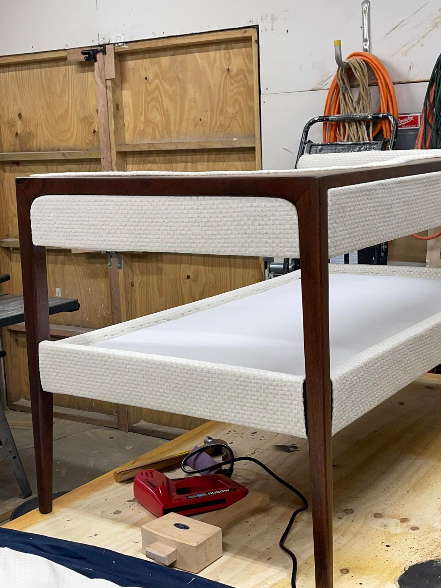 Two-tiered table with white woven sides and dark wood frame in a workshop. A red tool and a wooden block sit on a table.