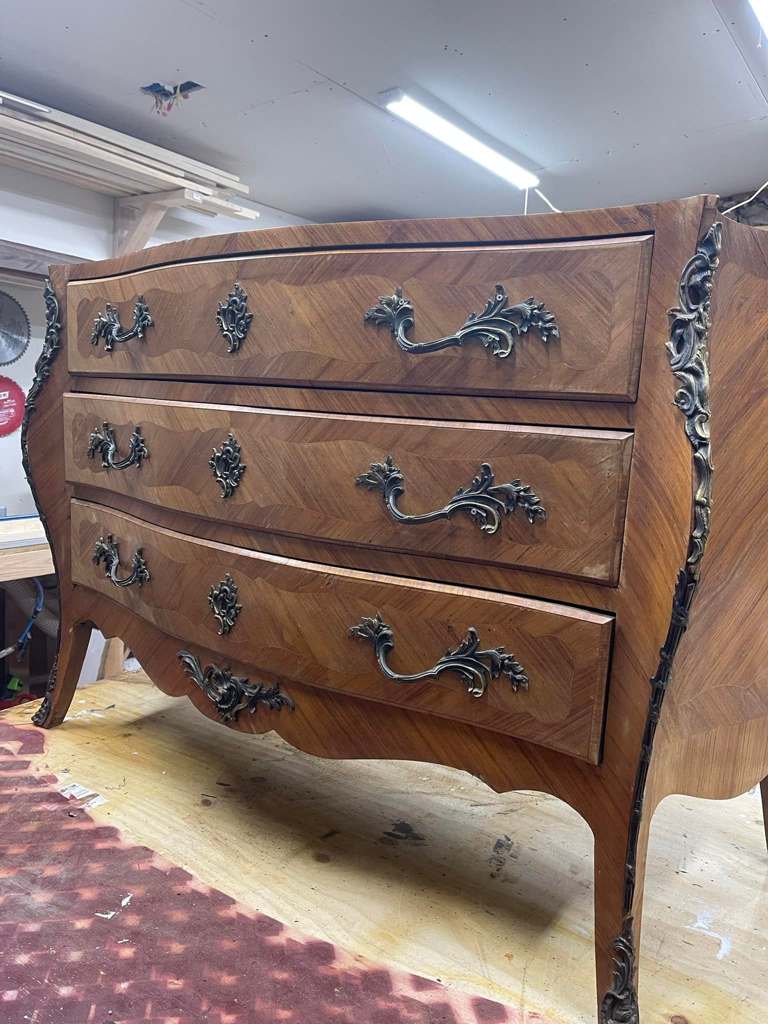 Antique wooden dresser with three drawers, ornate bronze hardware, curved front.