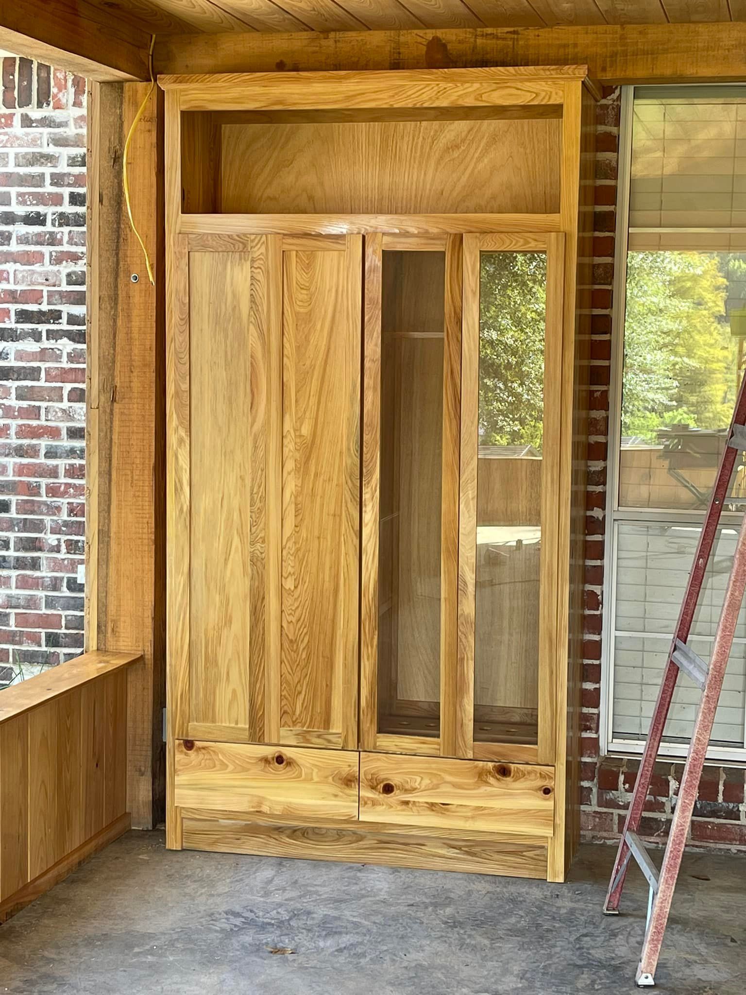 Wooden cabinet with two doors and glass panels on a porch, next to a brick wall.