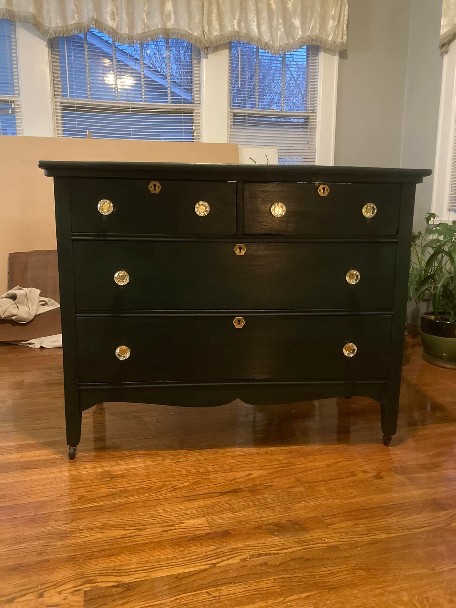 Black dresser with gold knobs, in front of a window.