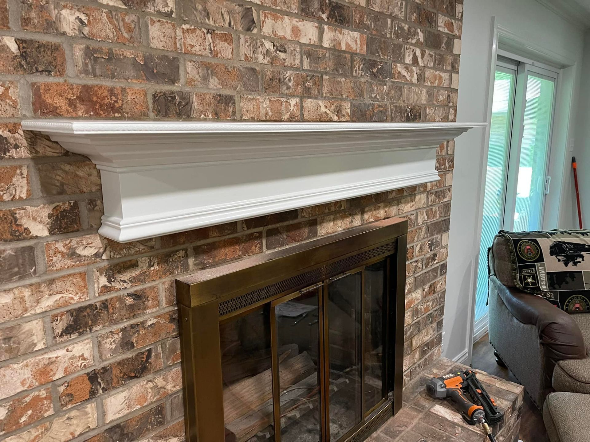 White fireplace mantel on brick wall, above a fireplace with a brass frame.
