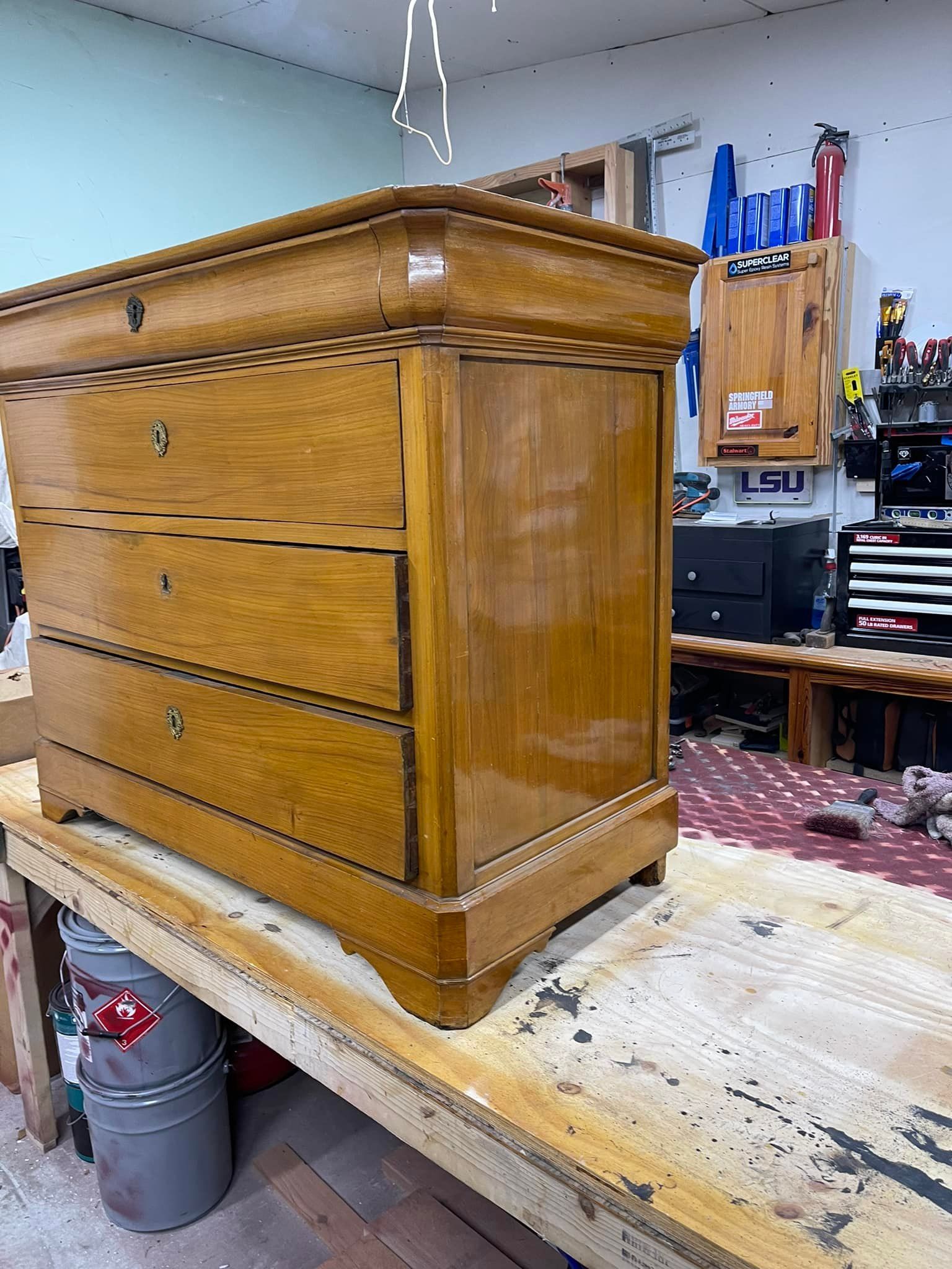 Wooden dresser on a workbench, in a workshop. The dresser has three drawers and a glossy finish.