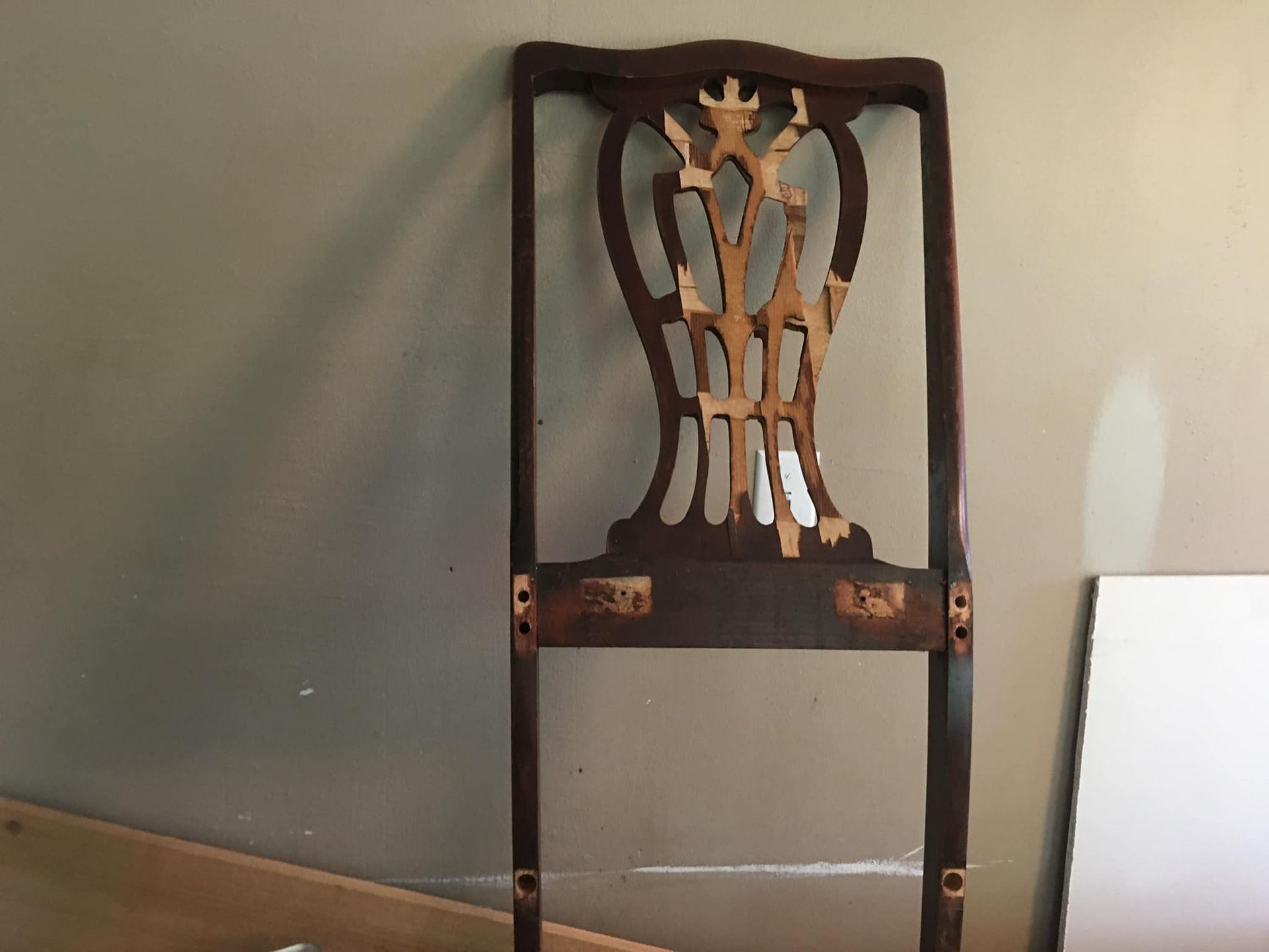 Brown wooden chair back with carved ornate design against a wall.