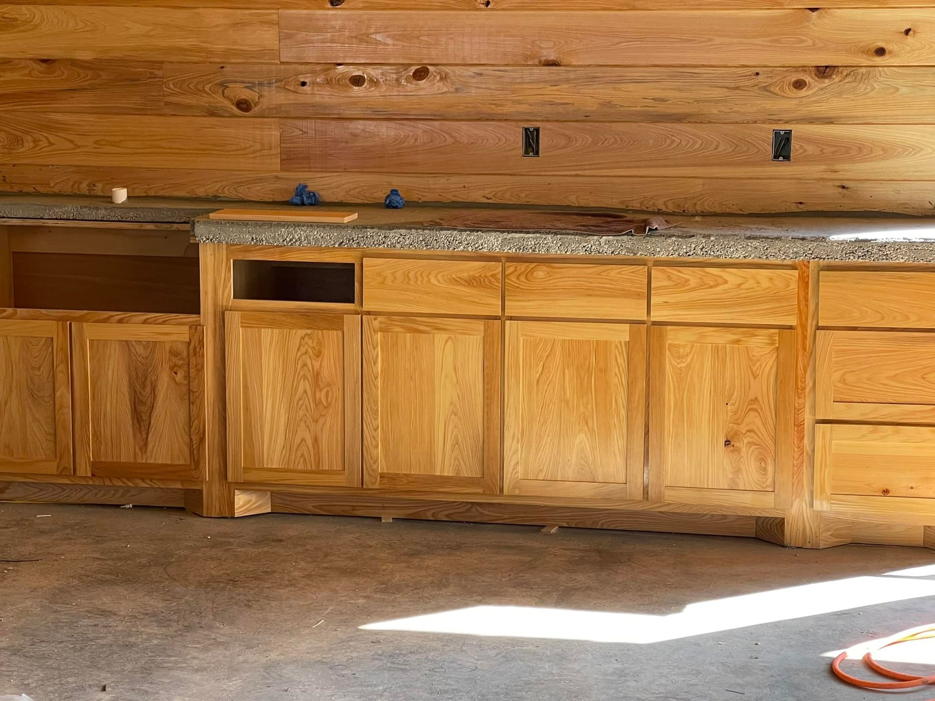 Wooden kitchen cabinets under a wooden wall with a speckled countertop.