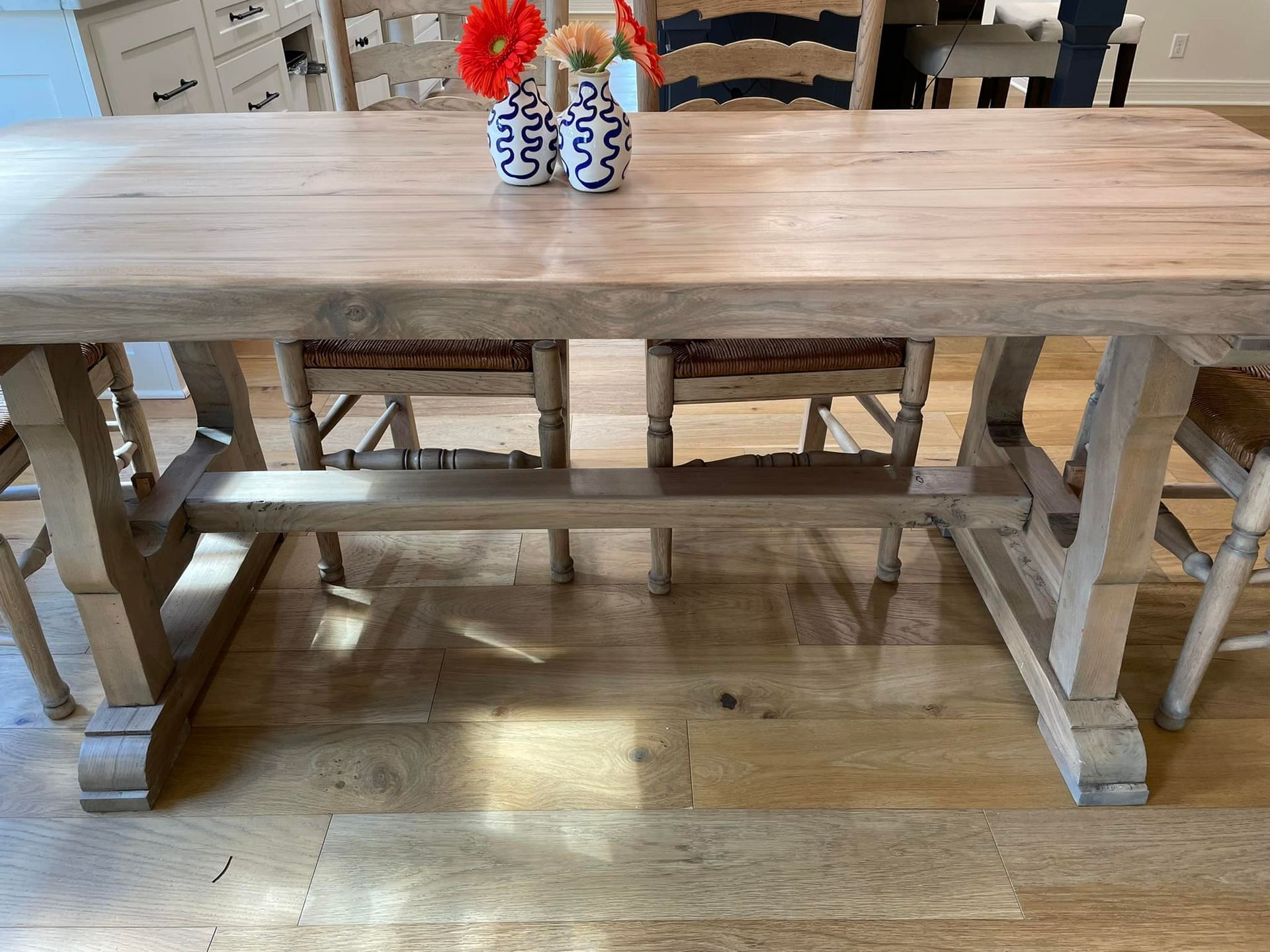 Light-wood dining table with four chairs, two vases with flowers, on hardwood floor.
