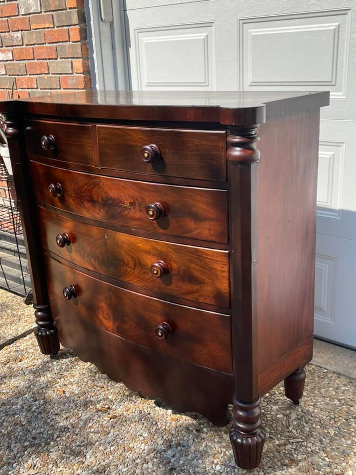 Dark wood dresser with five drawers and turned legs, set outside against a white door.