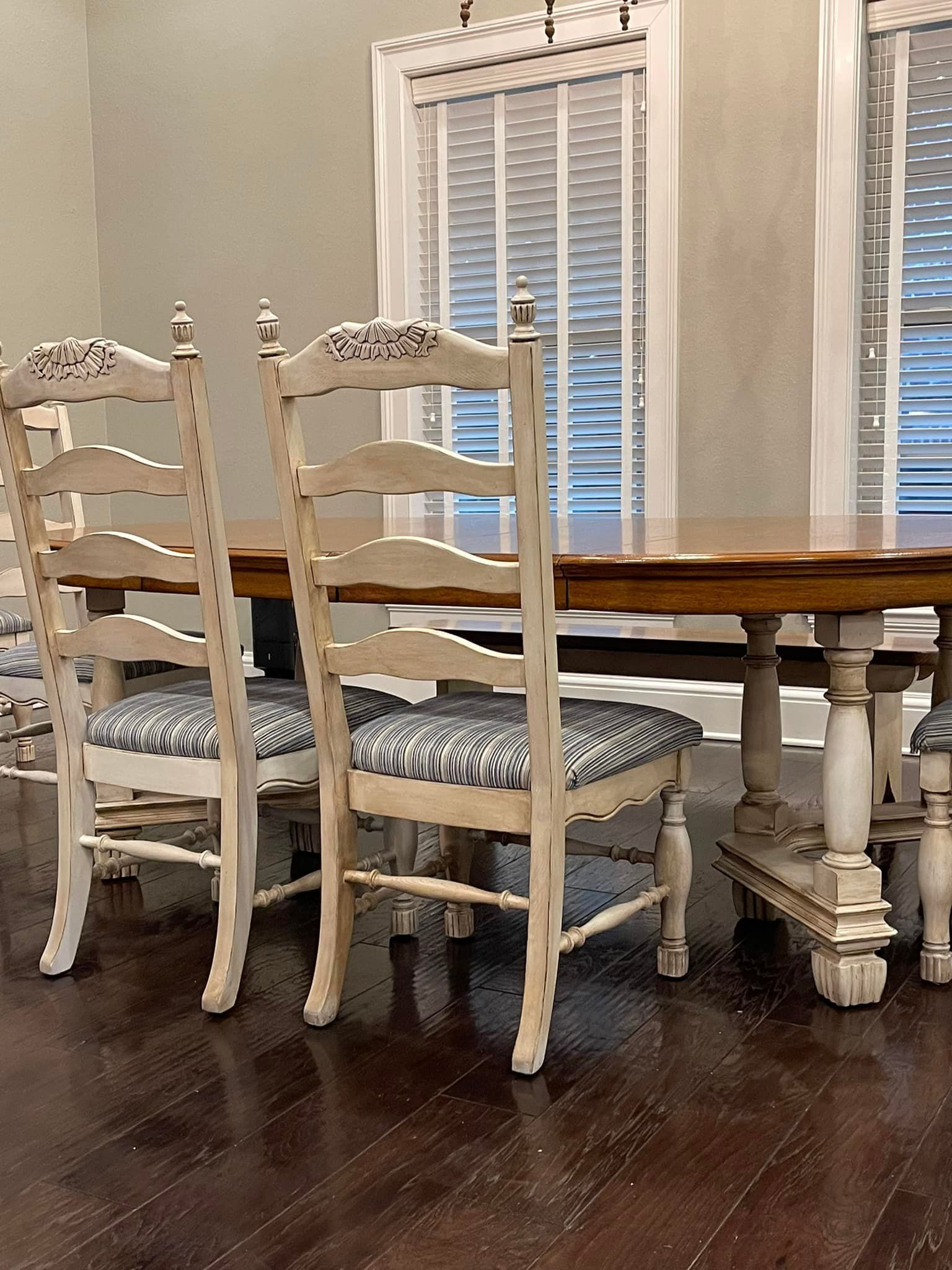Dining table with white chairs, blue patterned seats, and a wood tabletop, by a window.
