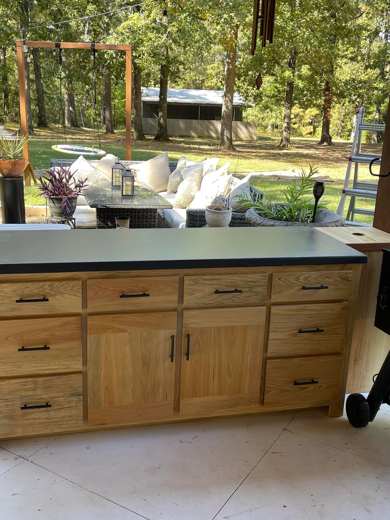 Outdoor kitchen with light wood cabinetry, dark countertop, and view of seating area.