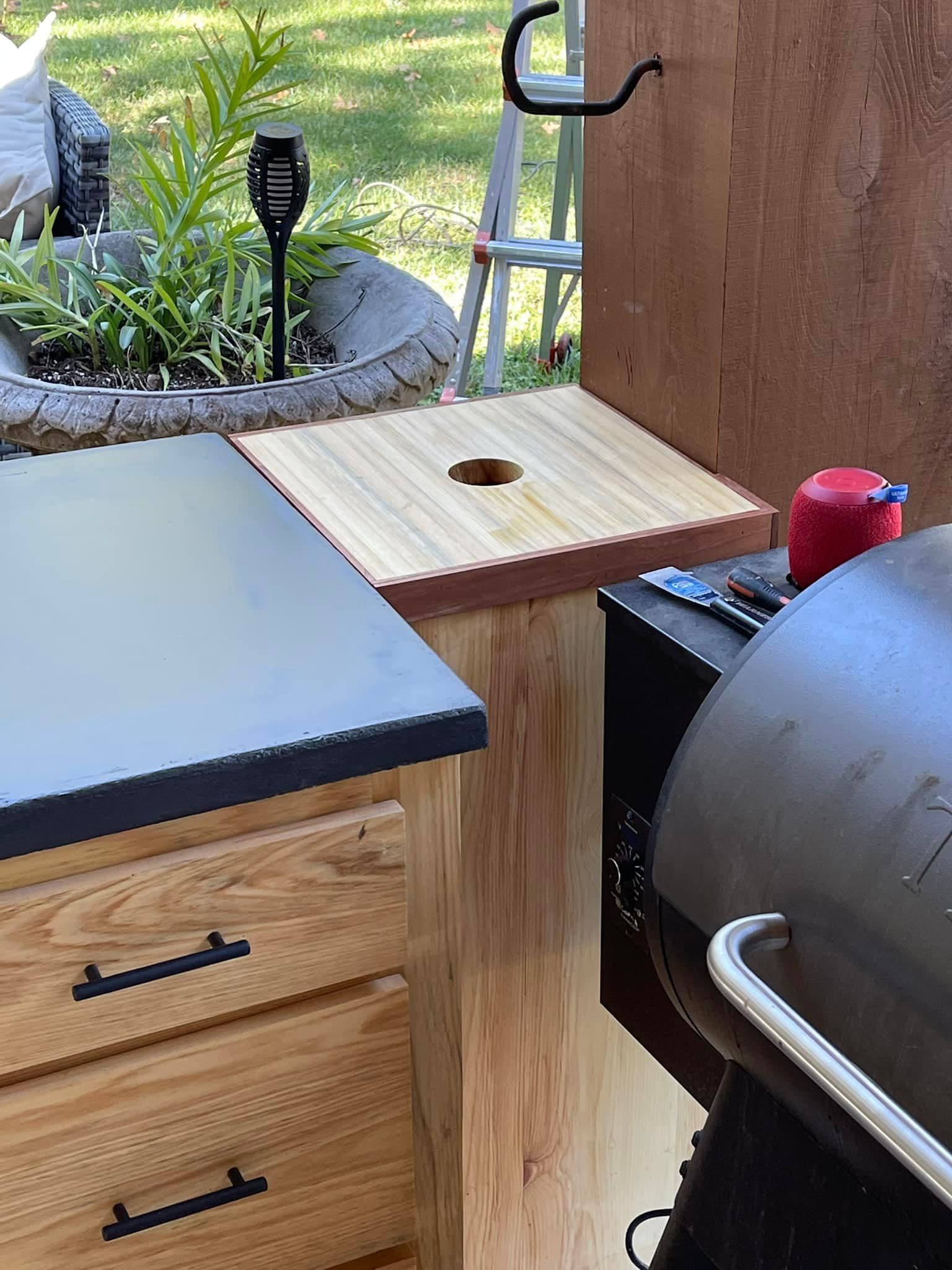 Outdoor kitchen with wooden cabinets, countertop, grill, and a cornhole board.