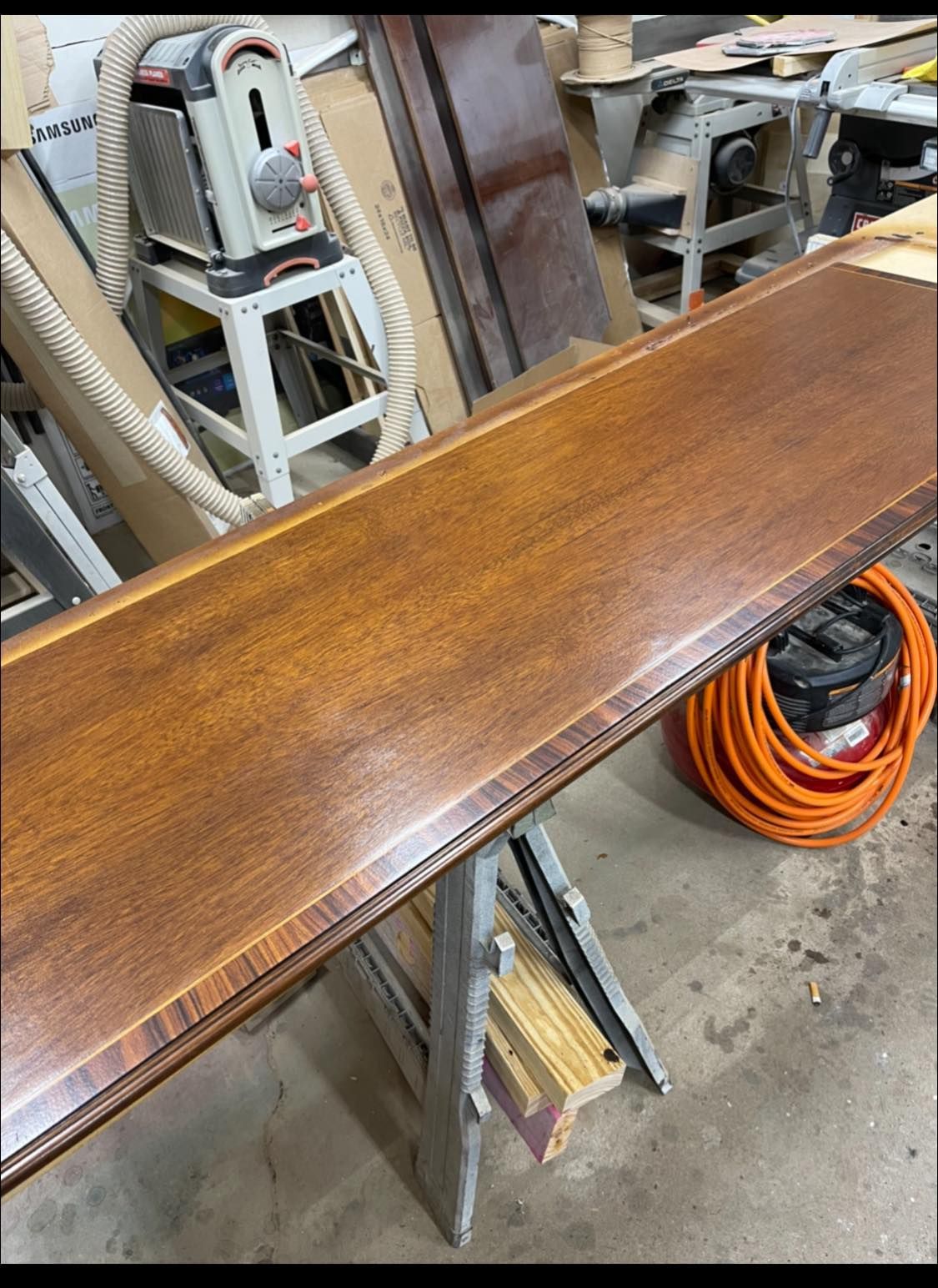 A long, wood piece with a glossy finish on a sawhorse in a workshop.