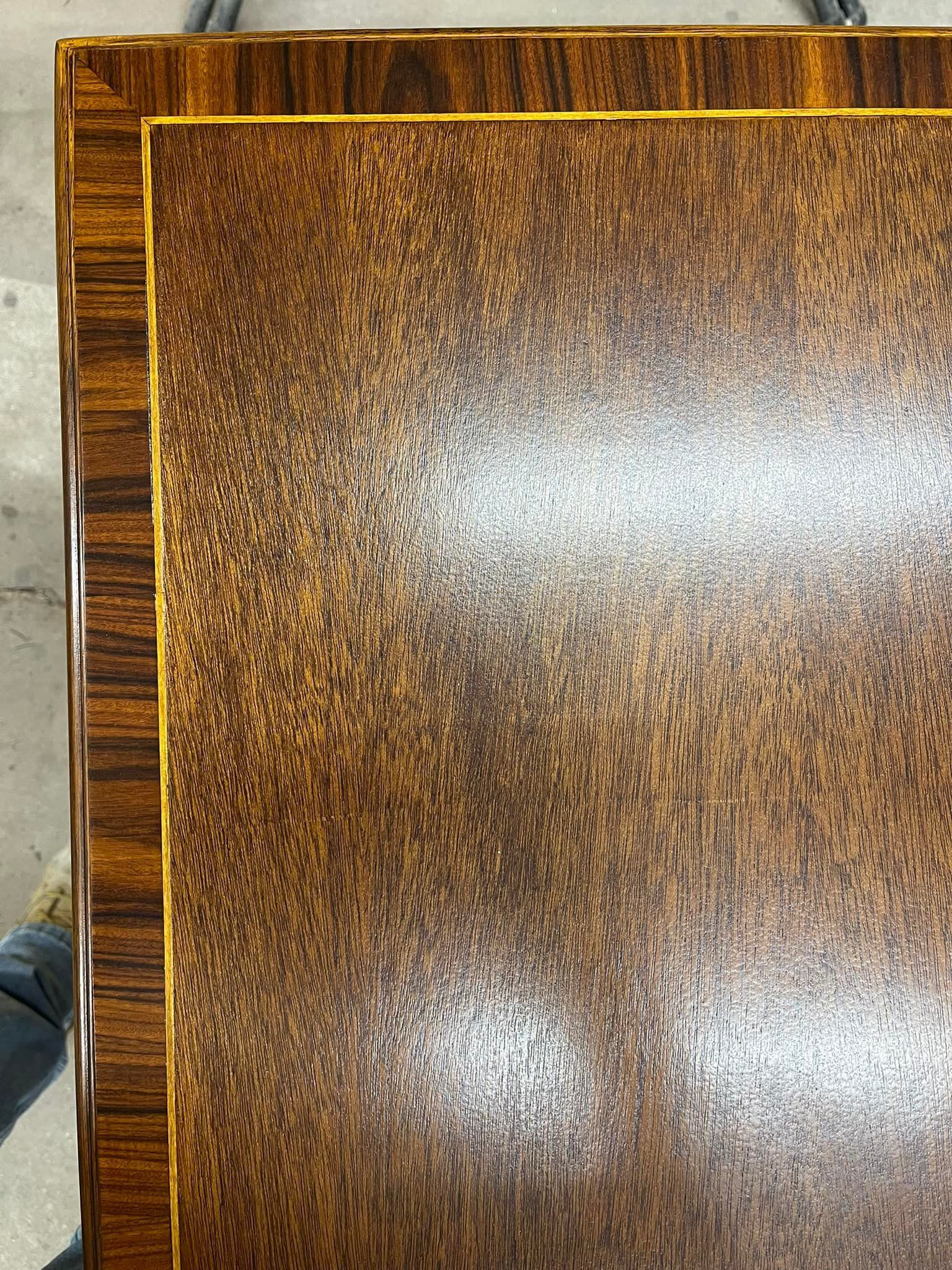 Close-up of a wooden table with a glossy finish. The top is a patterned brown color, with a darker brown trim.