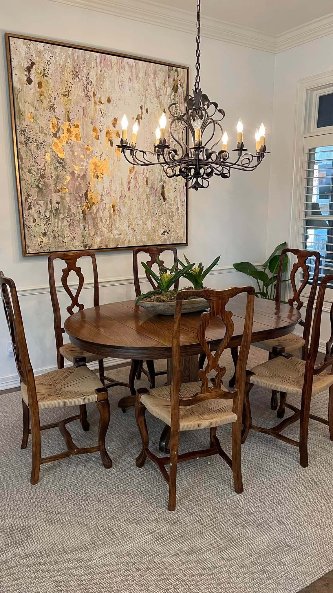 Dining room with oval wooden table, six chairs, rug, chandelier, and abstract art.