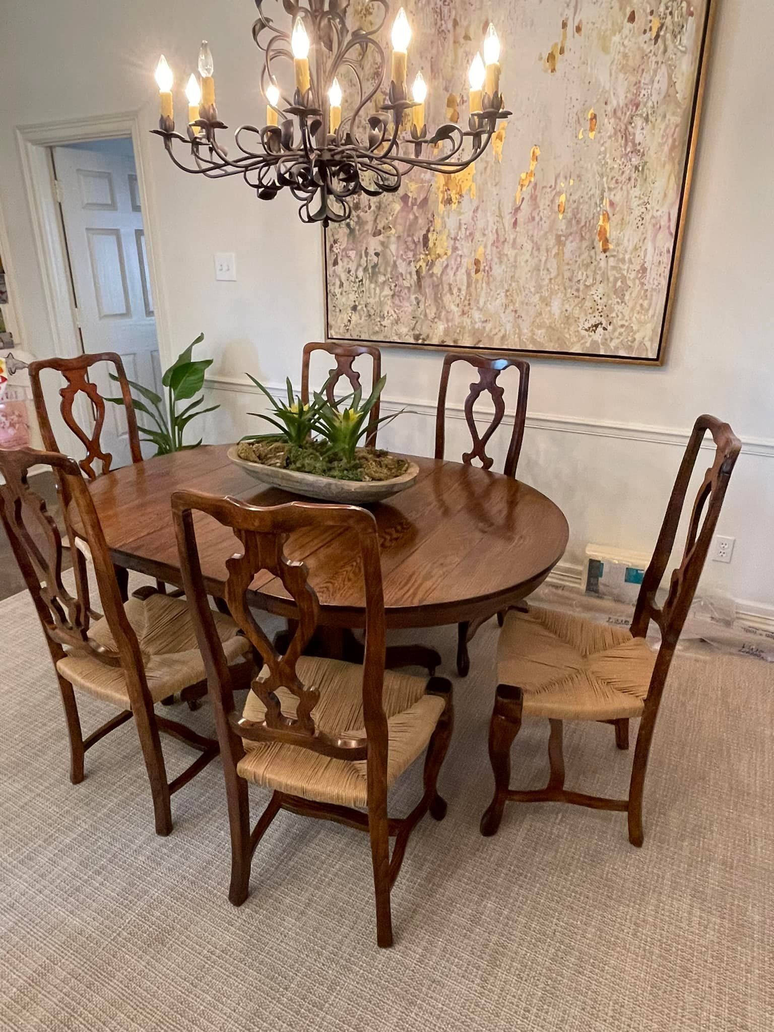 Dining room with a round wooden table, chairs with straw seats, and a large chandelier.