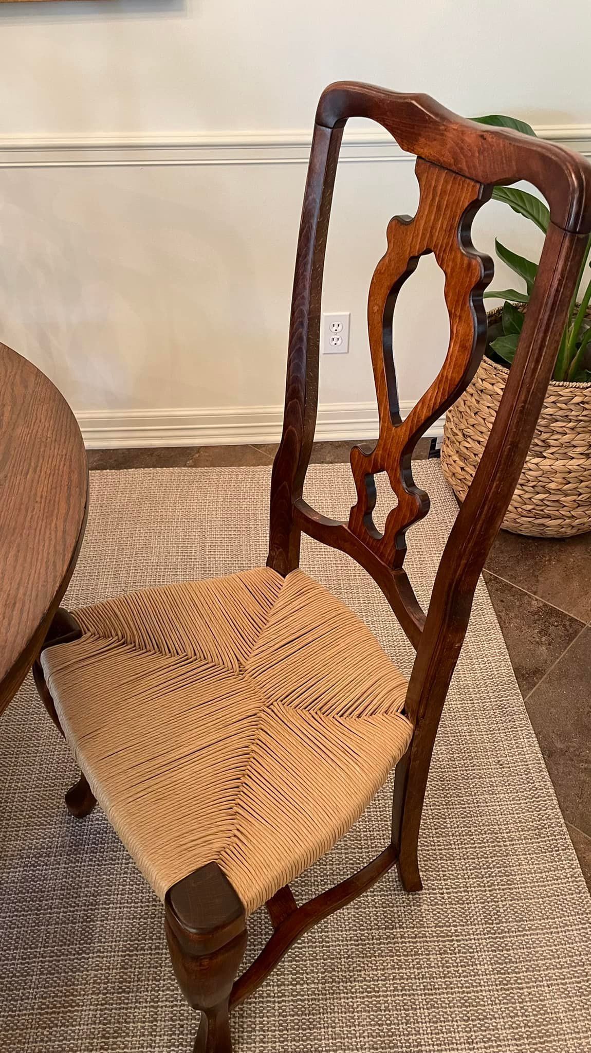 Wooden chair with intricately carved back and woven seat, on a rug.