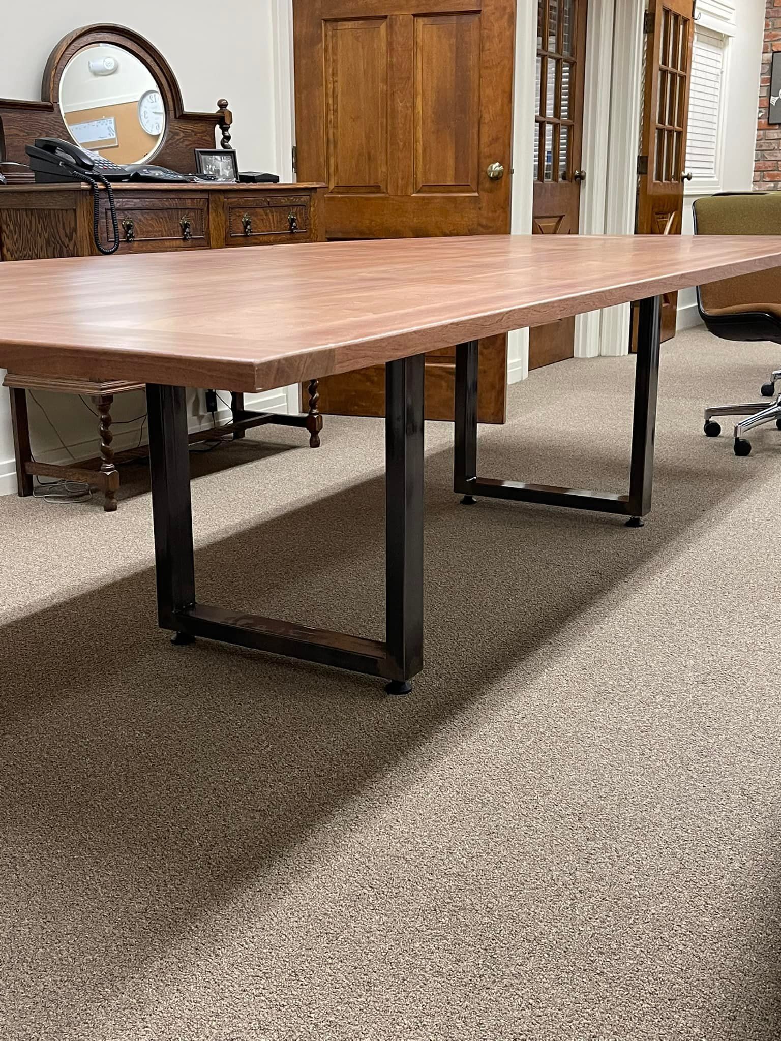 A large, rectangular brown table with black metal legs, set in an office space with a carpeted floor.
