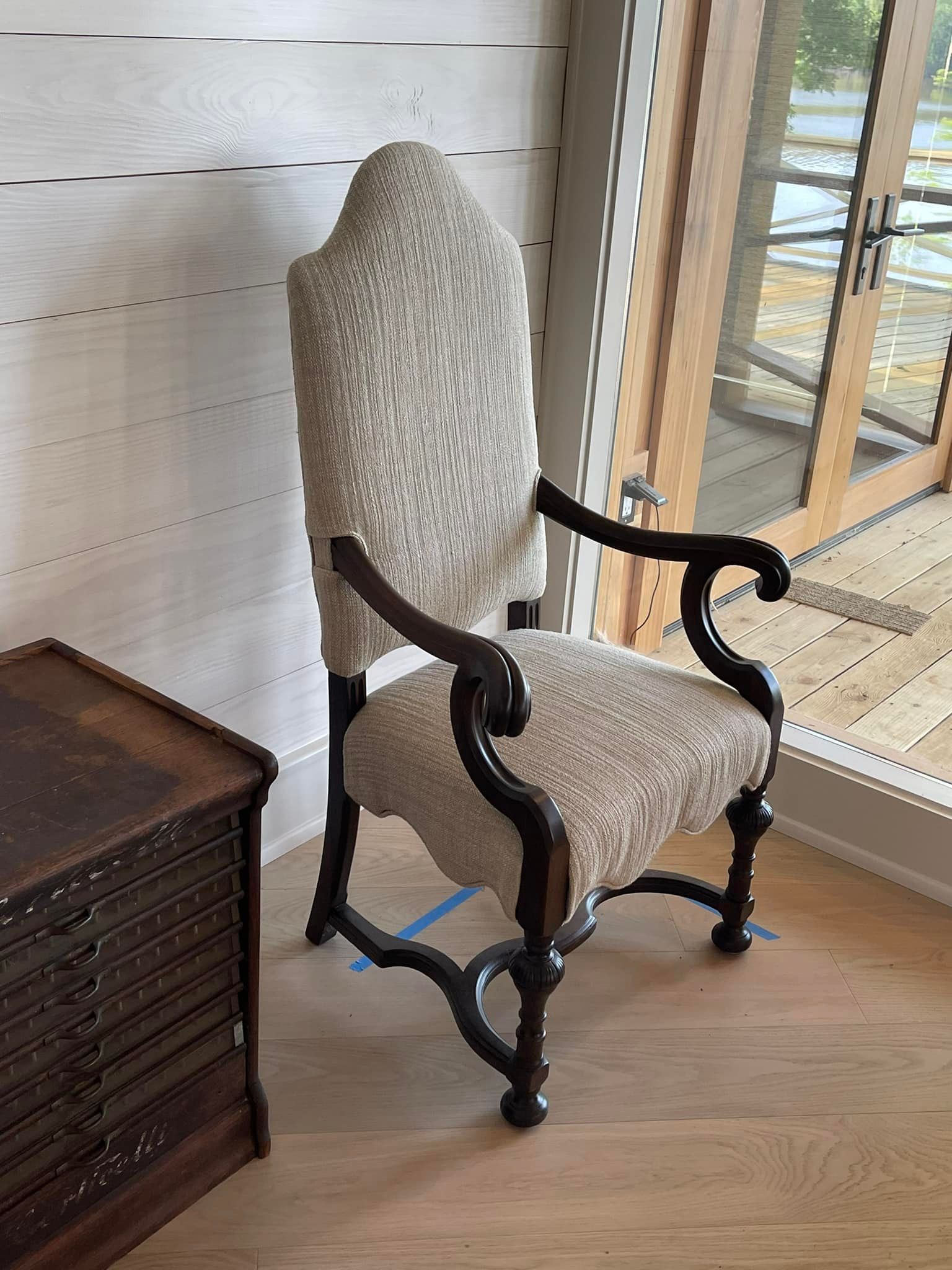 Upholstered armchair with dark wooden frame, next to a small wooden chest, and a sliding glass door.