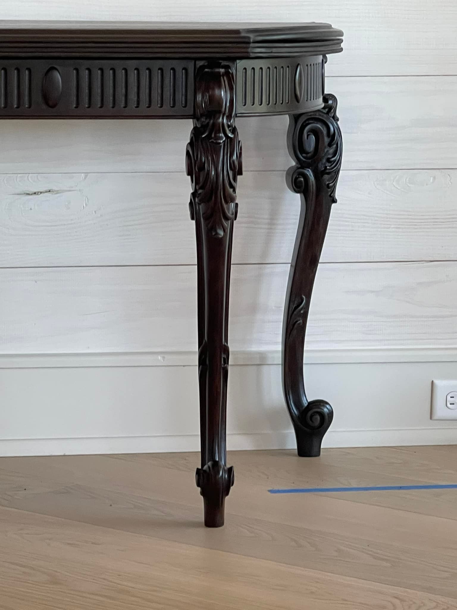 Dark wood console table with ornate carved legs against a white wall and wood floor.