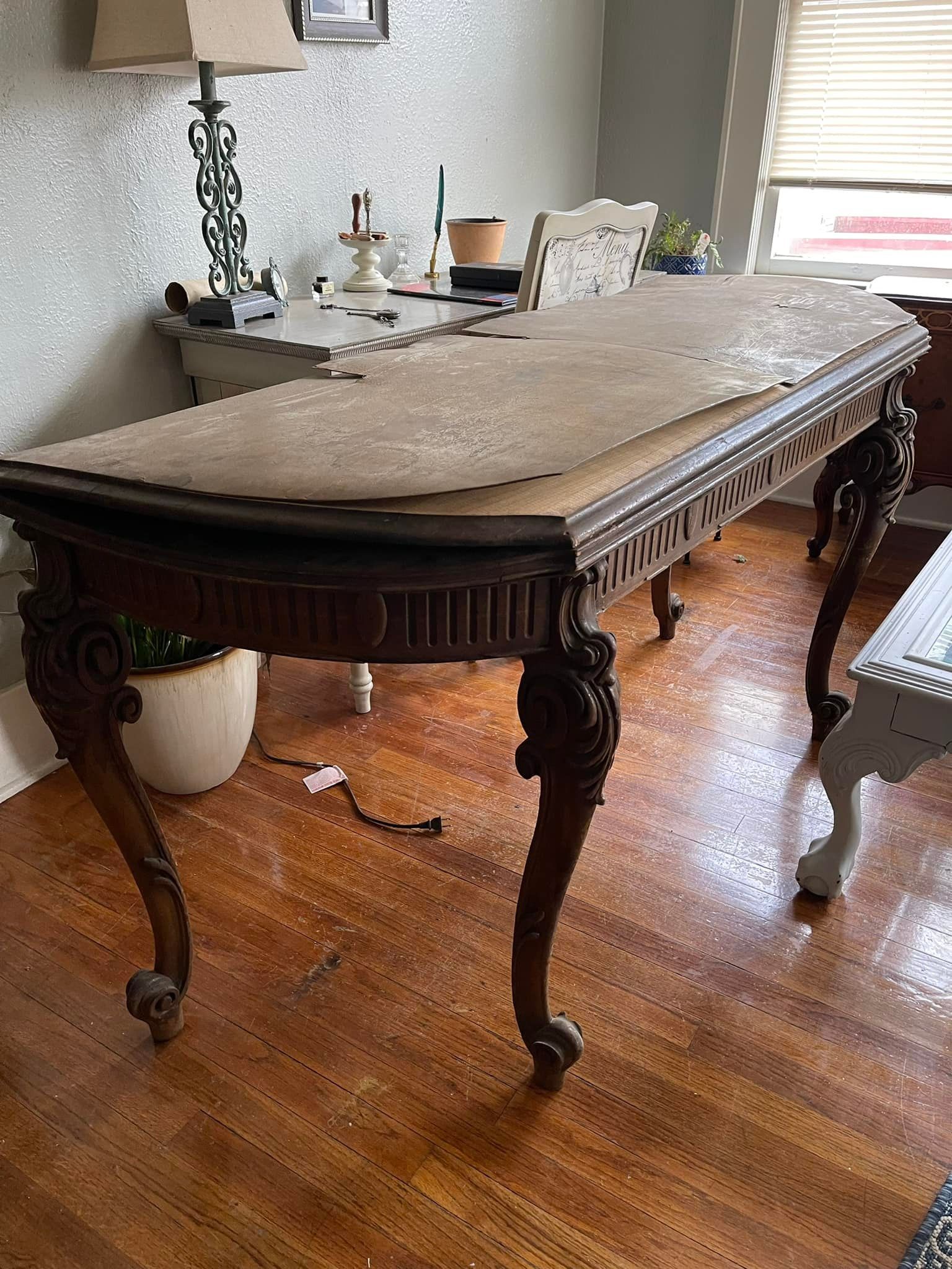 Antique wooden table with ornate carvings and a damaged top, in a room with hardwood floors.