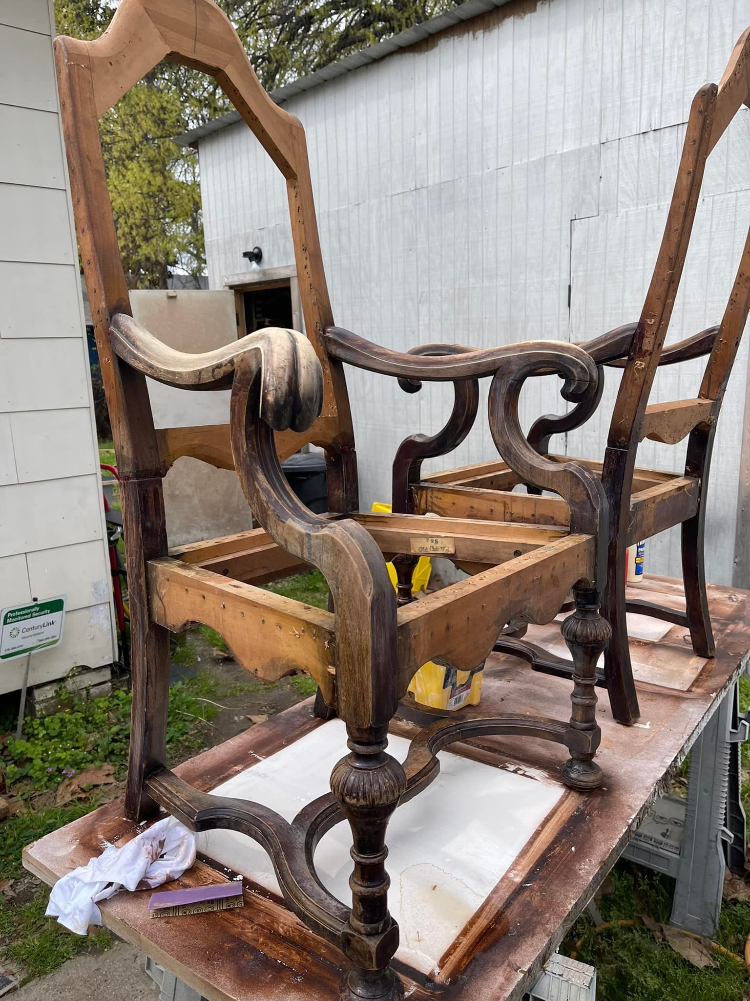 Two wooden chairs in the process of being restored, outdoors on a table. One is mostly stripped.