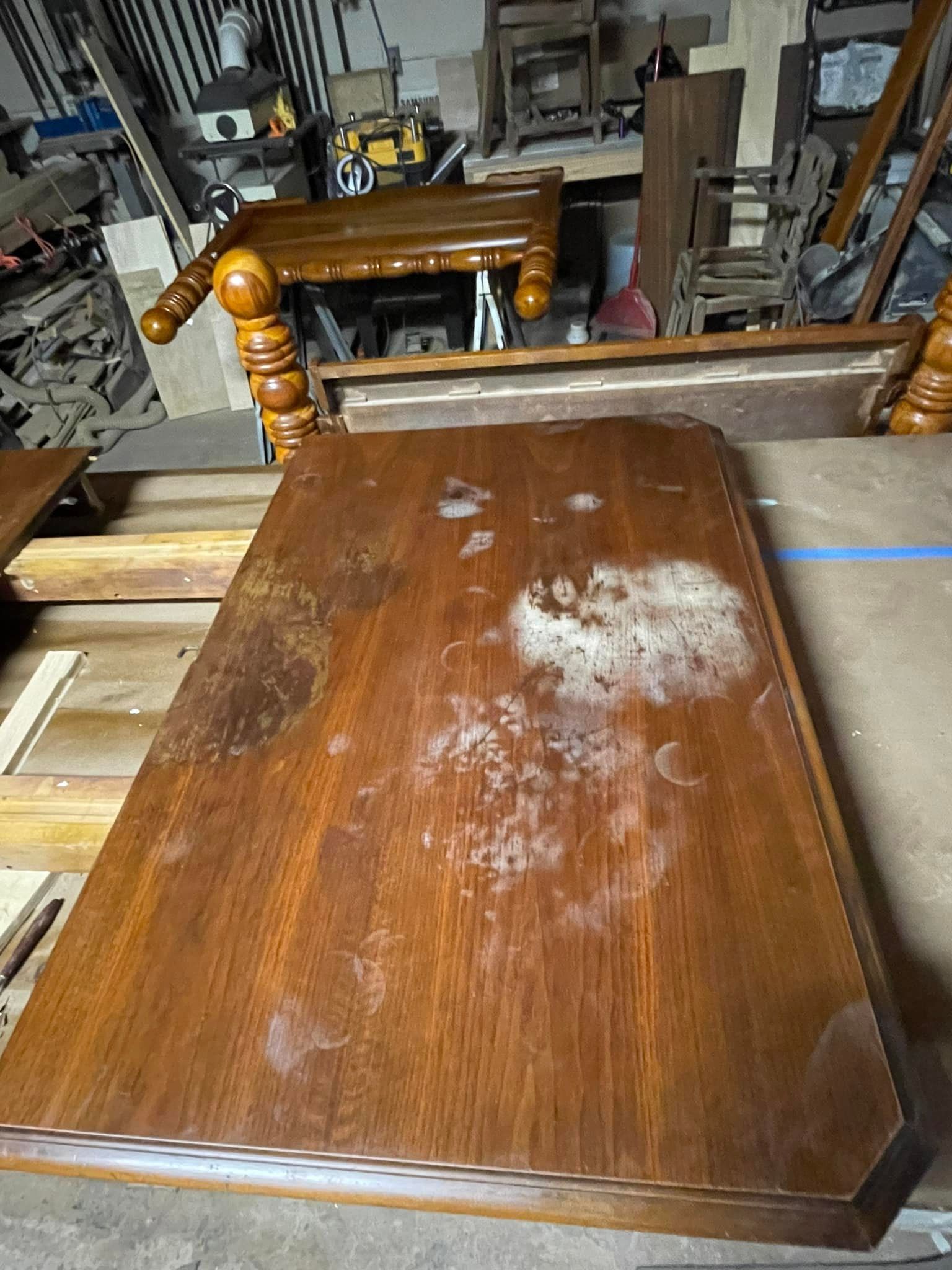Wooden table with worn finish and water stains in a workshop setting.