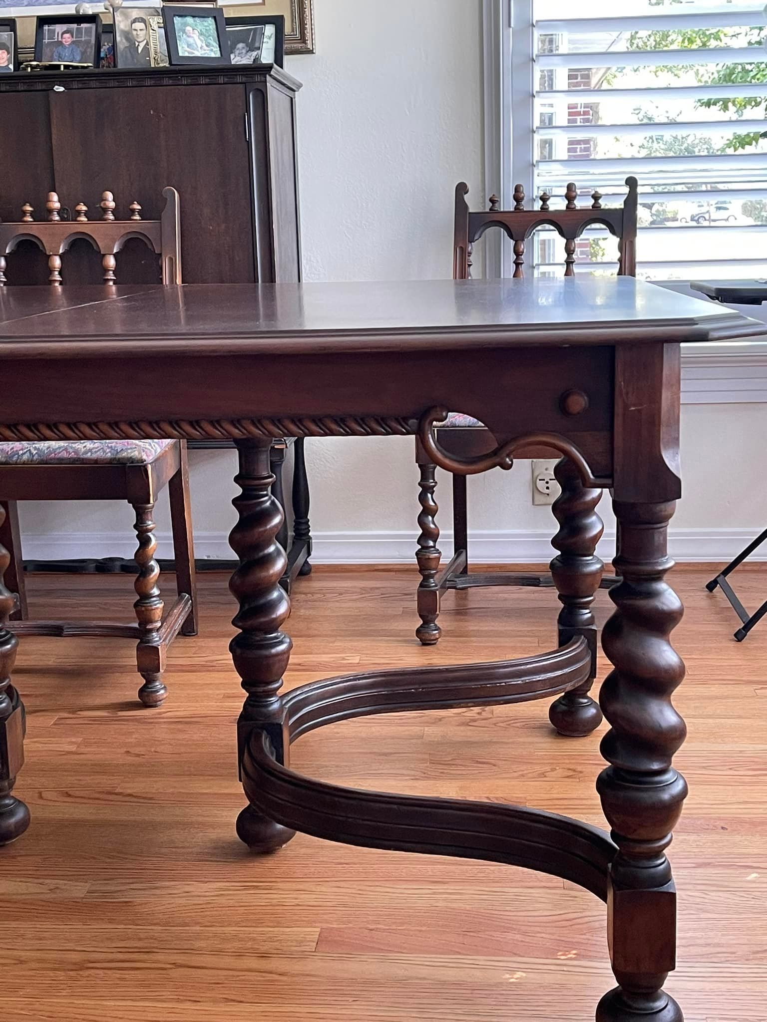 Dark wood dining table and chairs with spiral legs, set in a room with a piano and window.