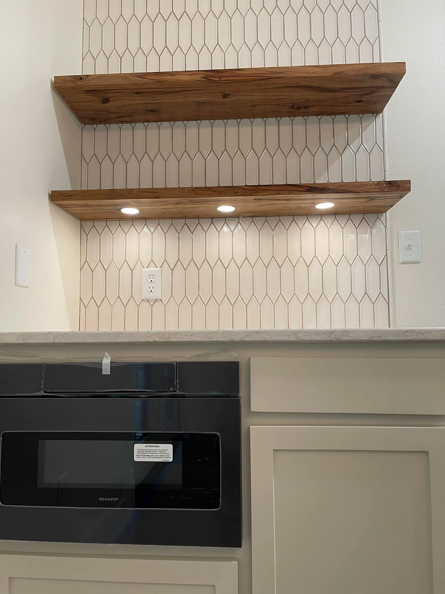 Two wooden shelves above a microwave, set against patterned off-white tile backsplash.