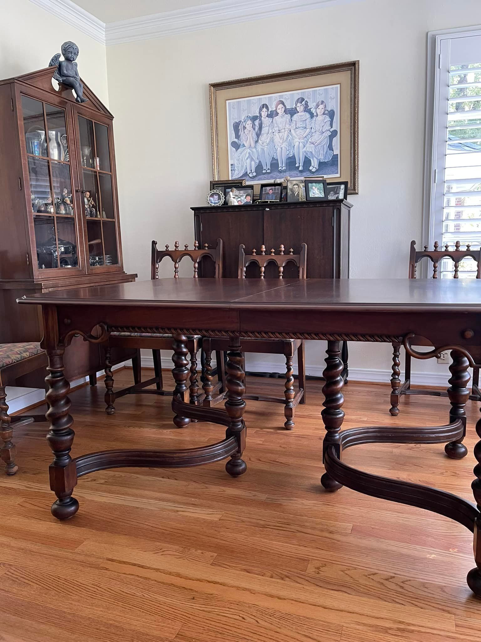 Wooden dining table and chairs in a room with a china cabinet, hardwood floors, and a framed photograph.