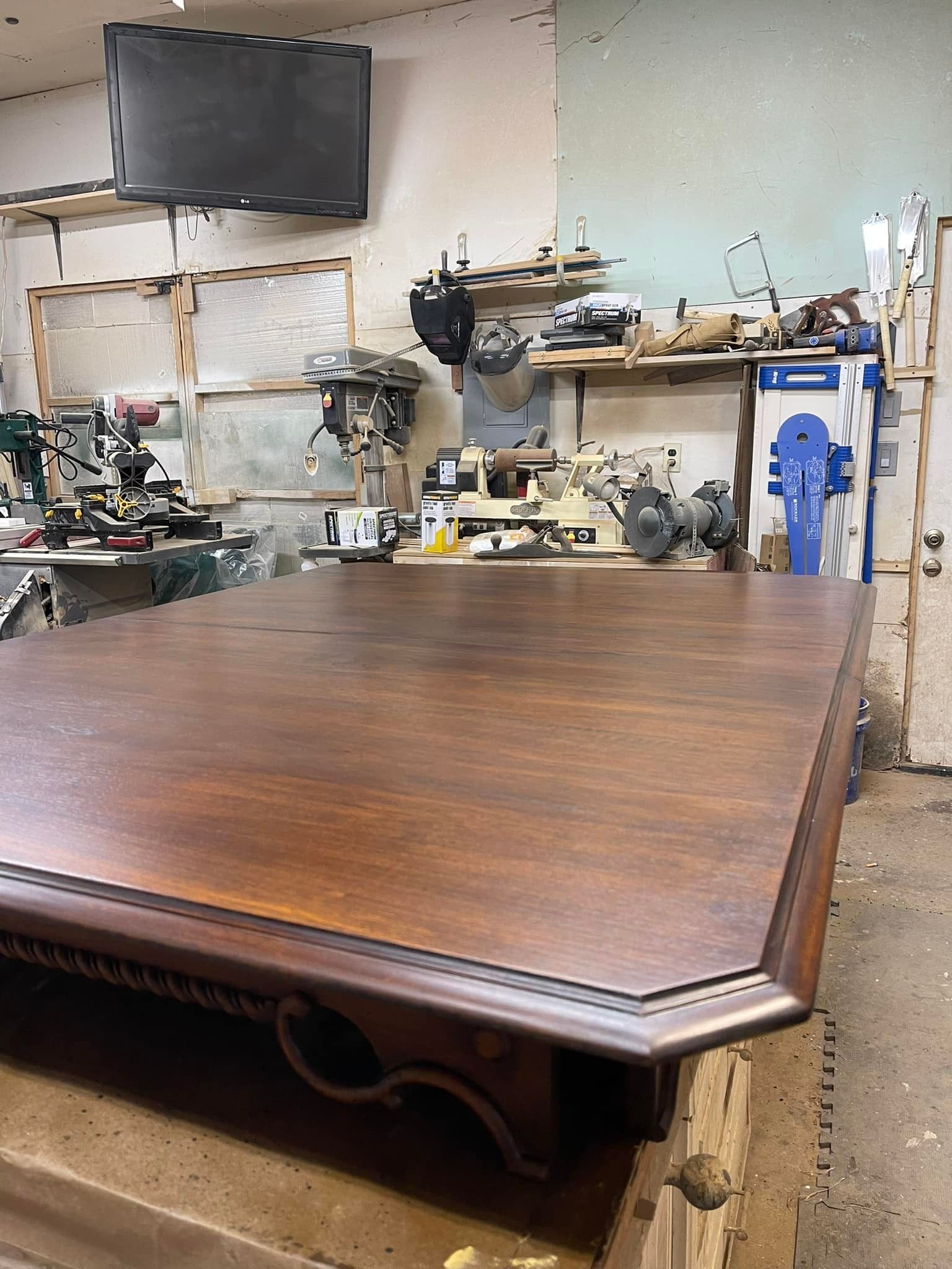 Large, dark wood table in a workshop, with tools and shelves in the background.