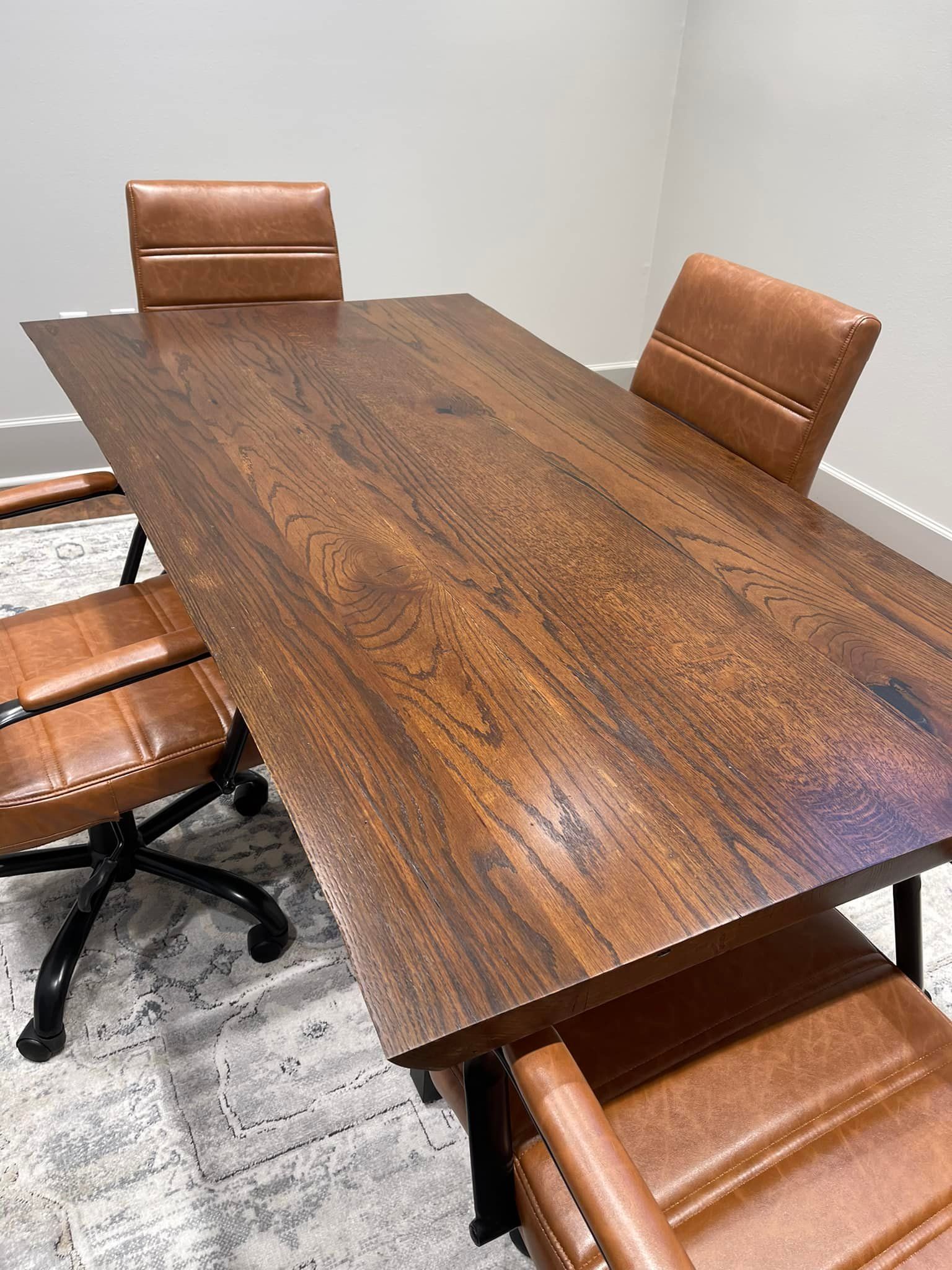 Wooden conference table with four brown leather chairs in a well-lit room.