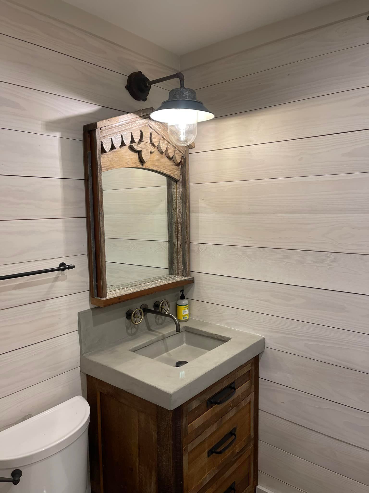 Small bathroom with wooden vanity, concrete sink, ornate mirror, and ship-style wall lamp.