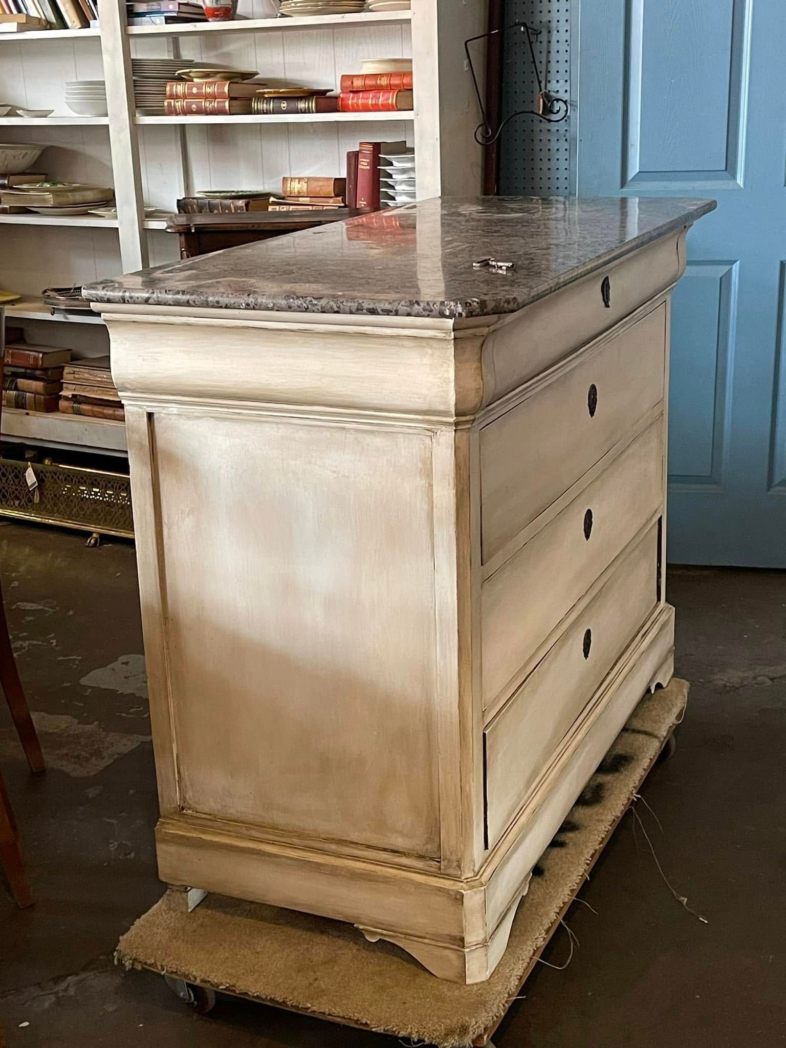Cream-colored kitchen island with granite top and drawers, sitting on a pallet in a shop.