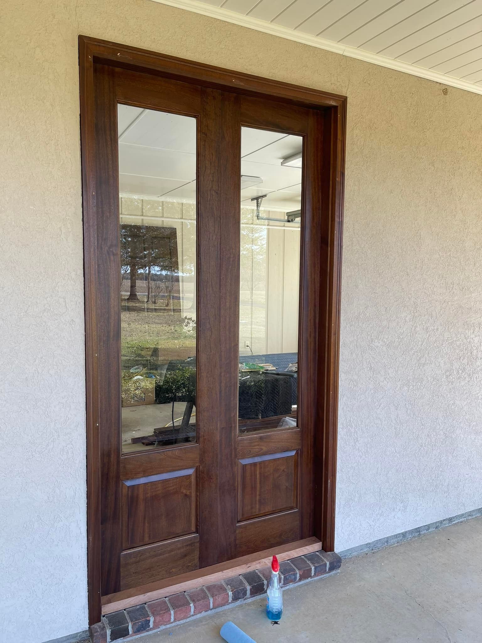 Double glass doors with dark brown wood frame, set in stucco wall.