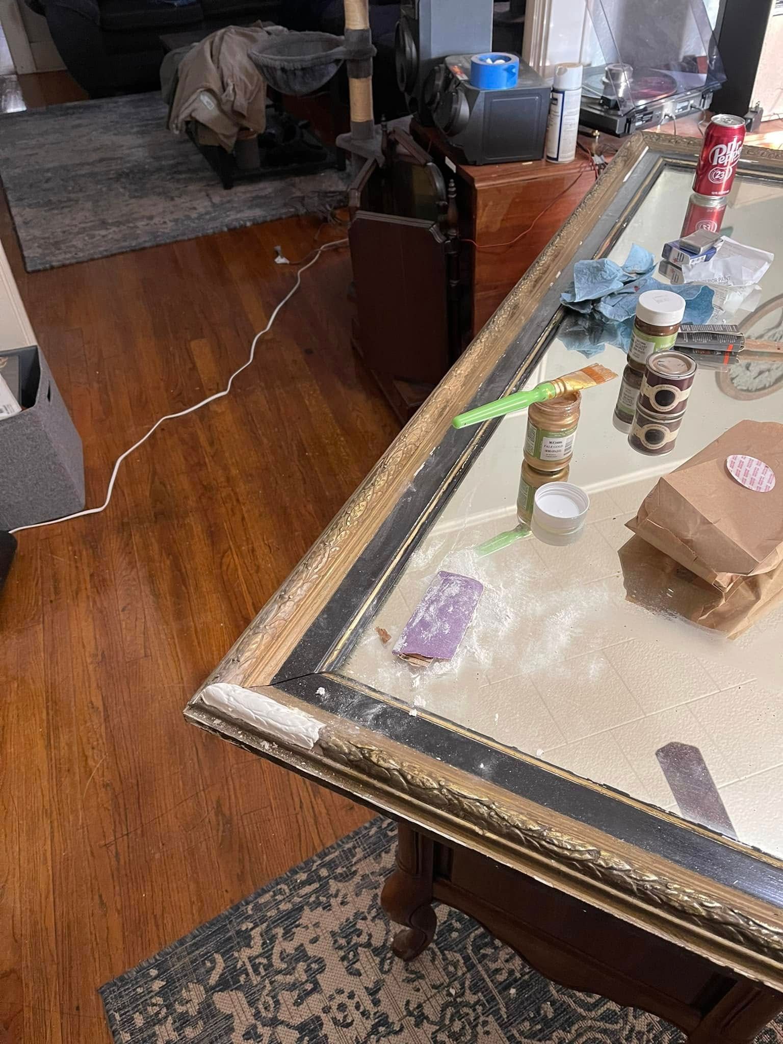 Mirror-topped table with gold and black trim, holding objects like candles, a small bag, and a bottle. Wooden floor.