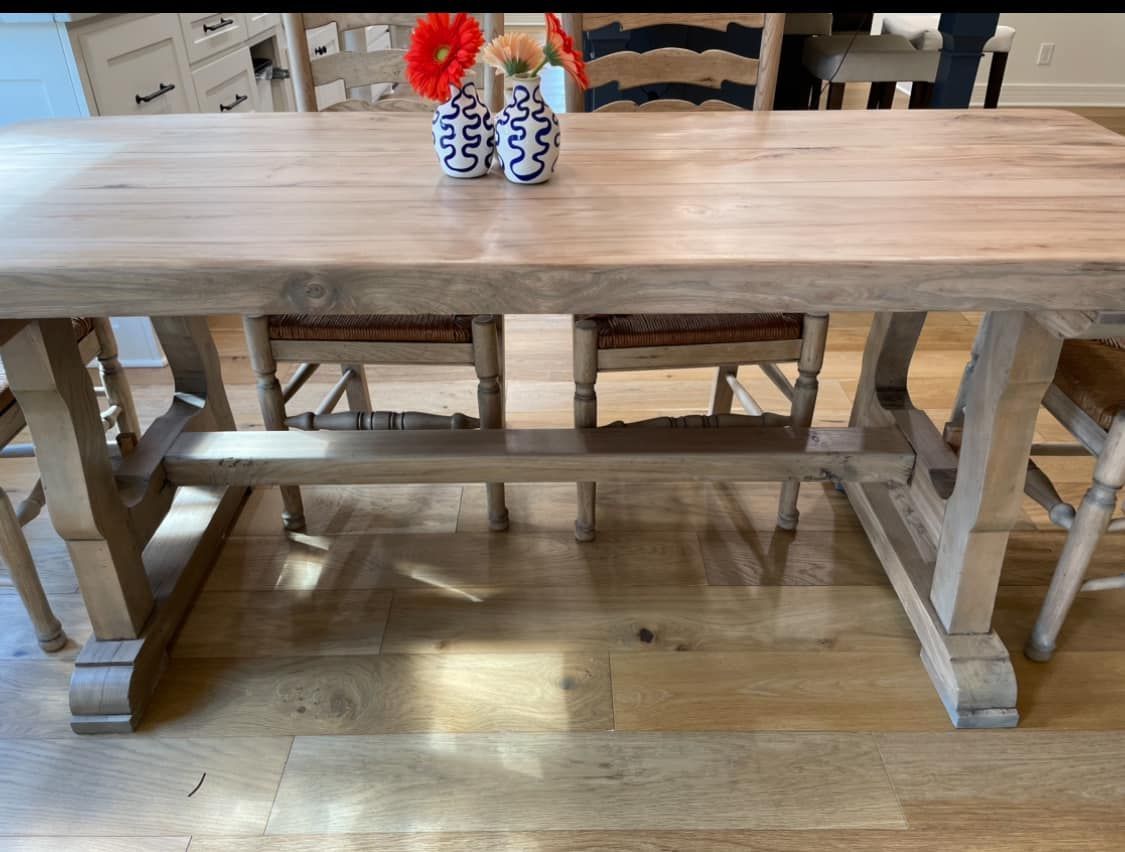 Wooden dining table with chairs and vase of flowers.