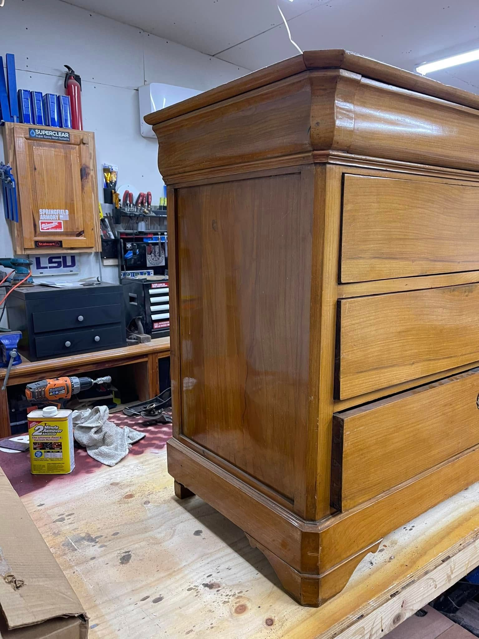 Wooden dresser being refinished in a workshop, drawers open, with tools and supplies visible in the background.