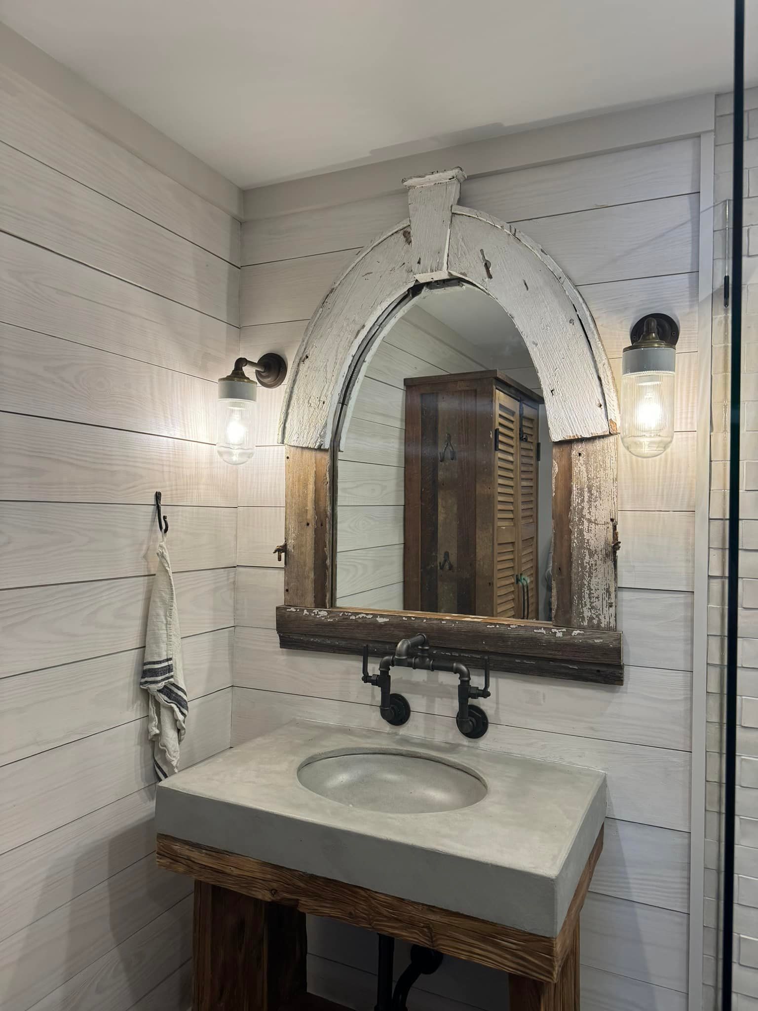Bathroom with rustic design; concrete sink, wood-framed mirror, two sconces, and shiplap walls.