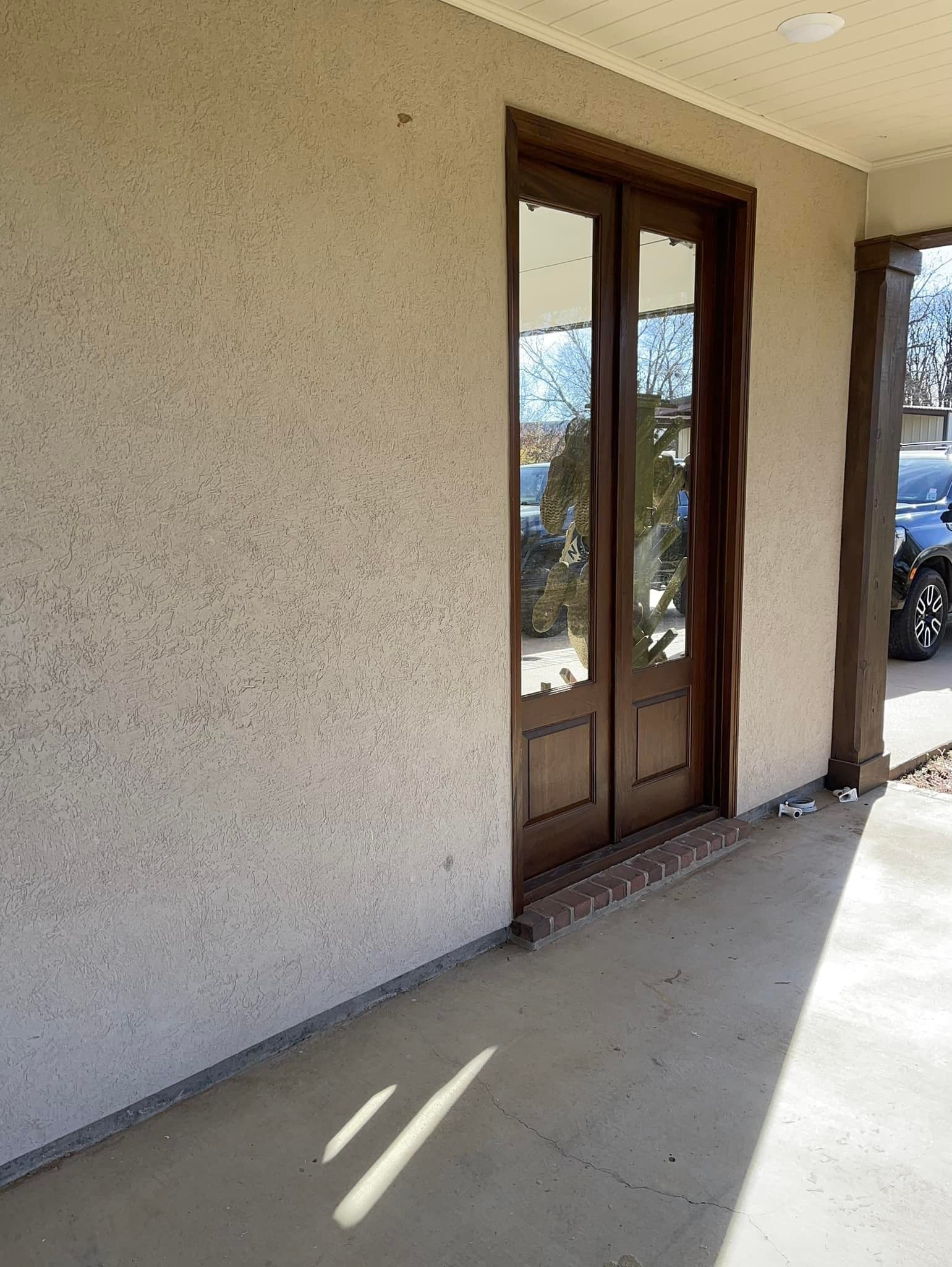 Exterior view of a building with double doors. Tan stucco wall, brown door frame, and concrete floor.