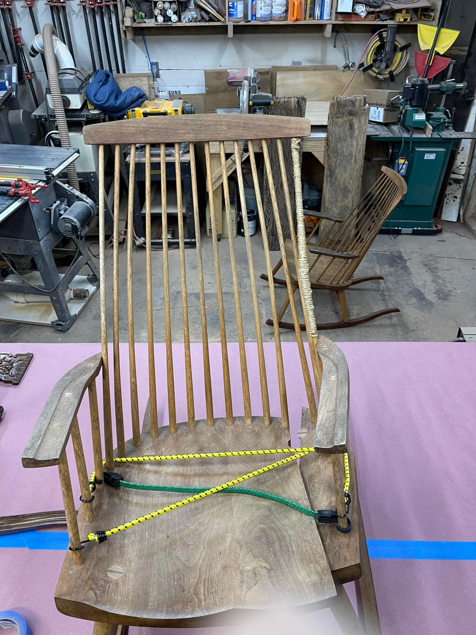 Old wooden chair with bungee cords holding it together, inside a workshop.