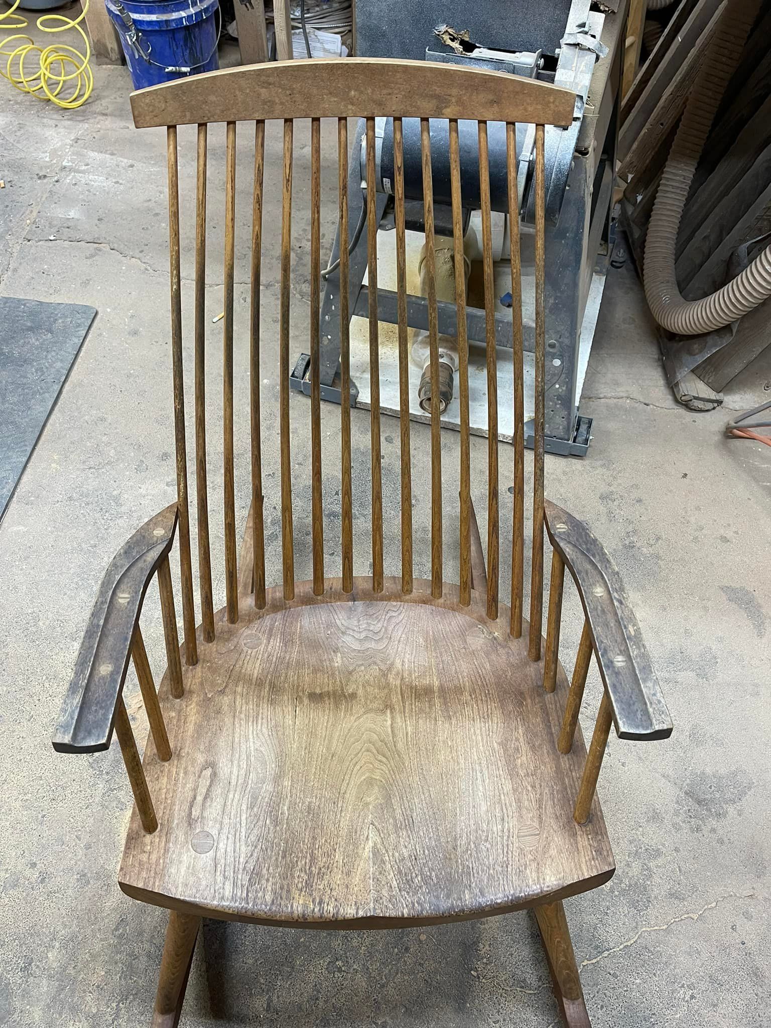 Wooden rocking chair with a tall back and spindles in a workshop.