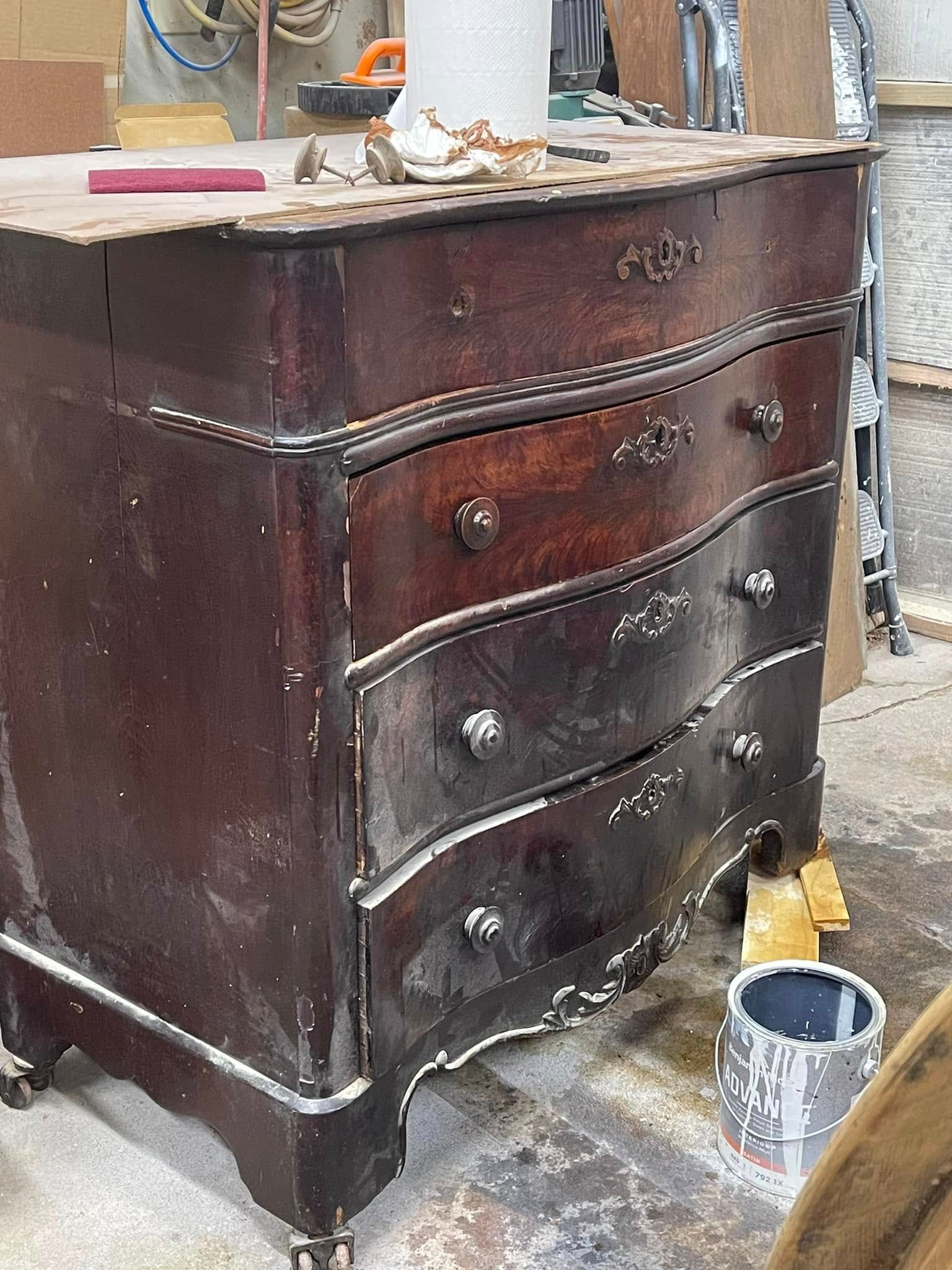 Dark wooden dresser with curved drawers and silver hardware, in a workshop setting.