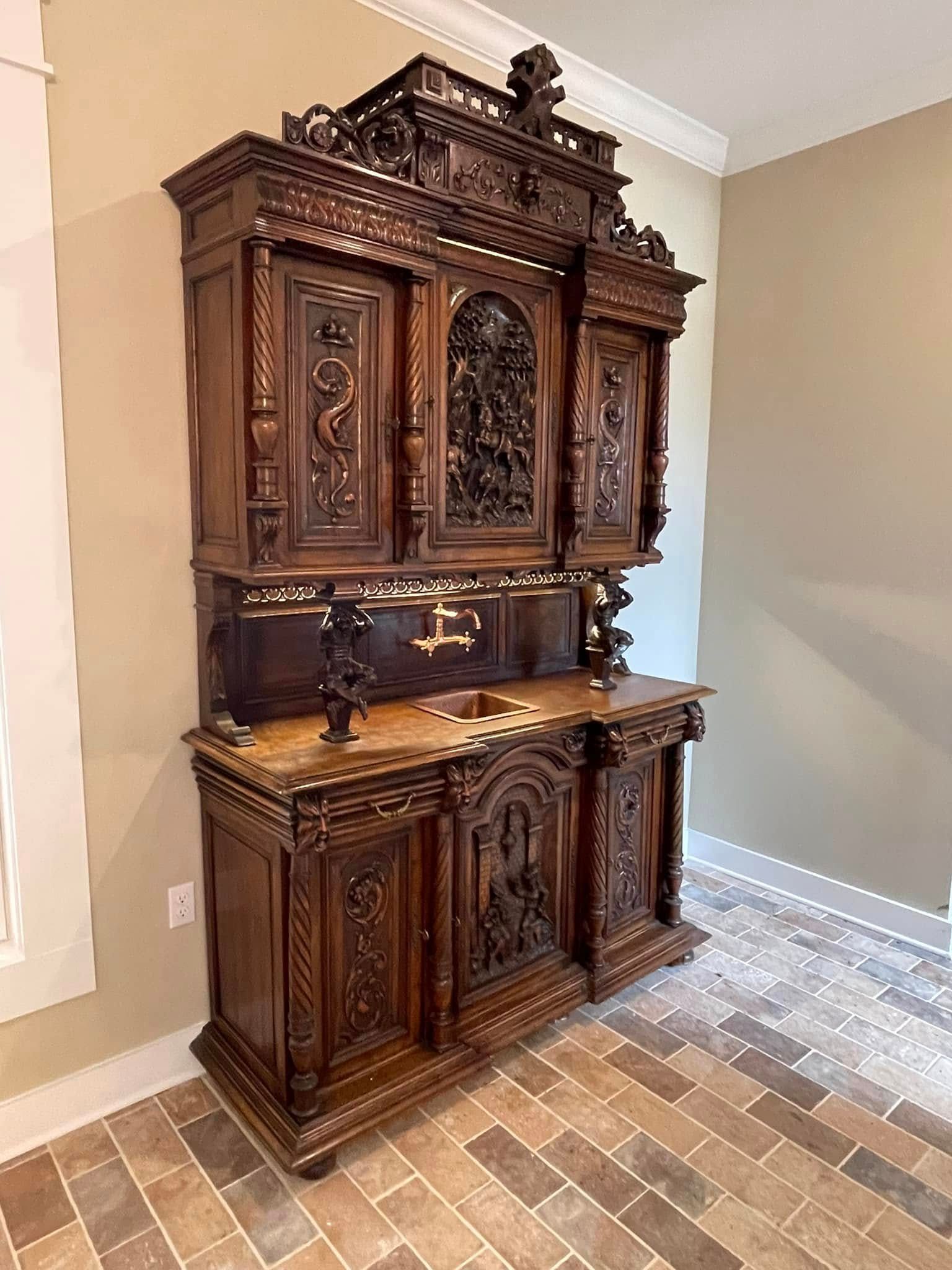 Dark wood ornate antique cabinet with carvings in a room with light brown walls and tile floor.