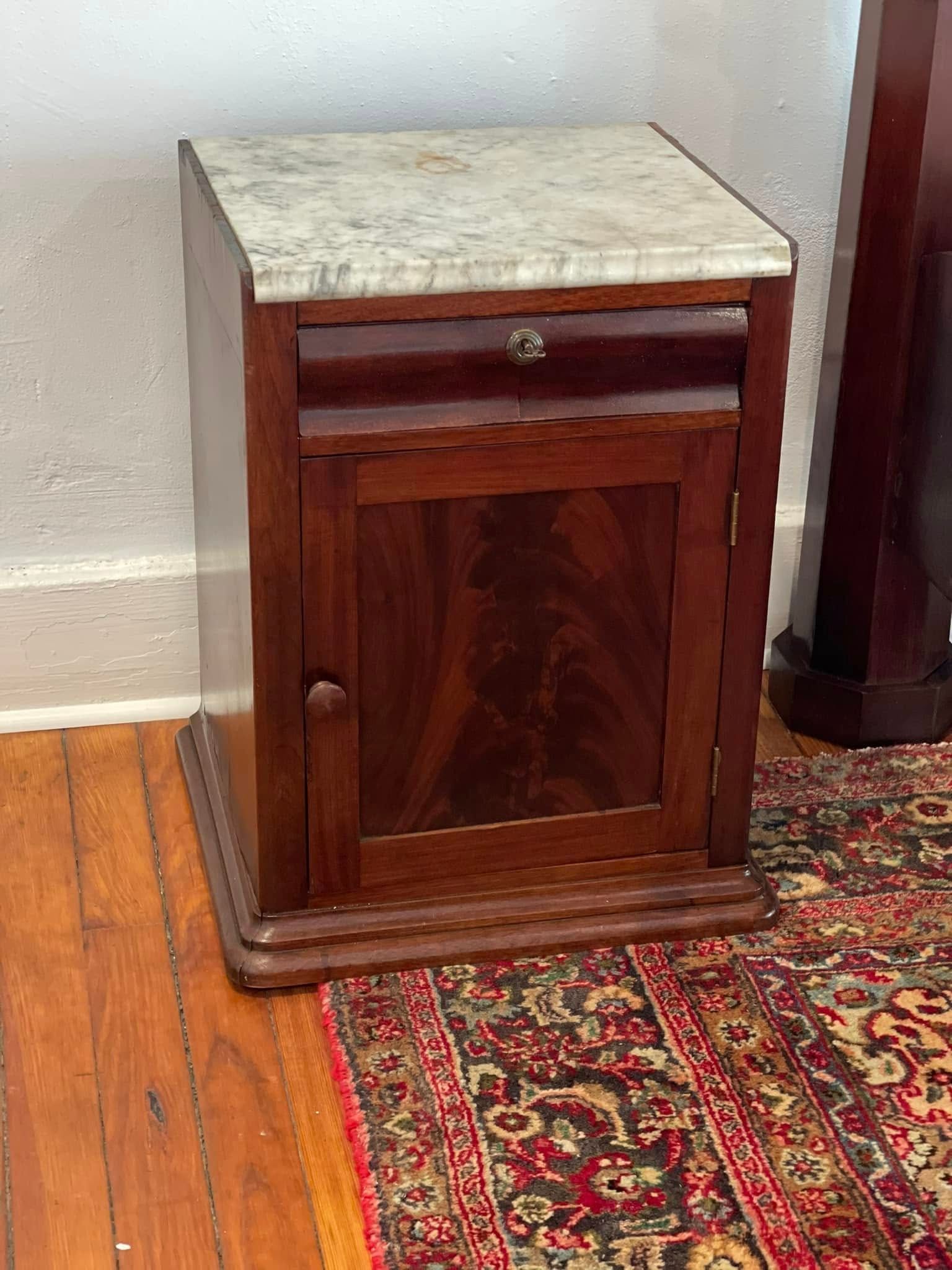 Dark wood bedside cabinet with marble top, drawer, and door, sitting on a patterned rug.