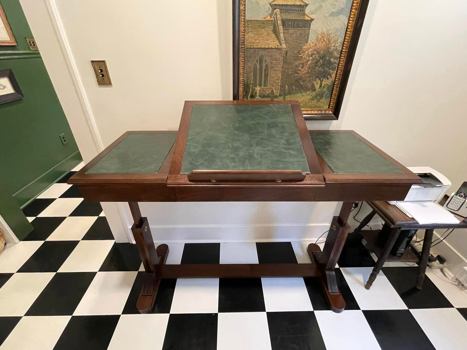 Wooden desk with green leather top, on black and white checkered floor, near a painting.