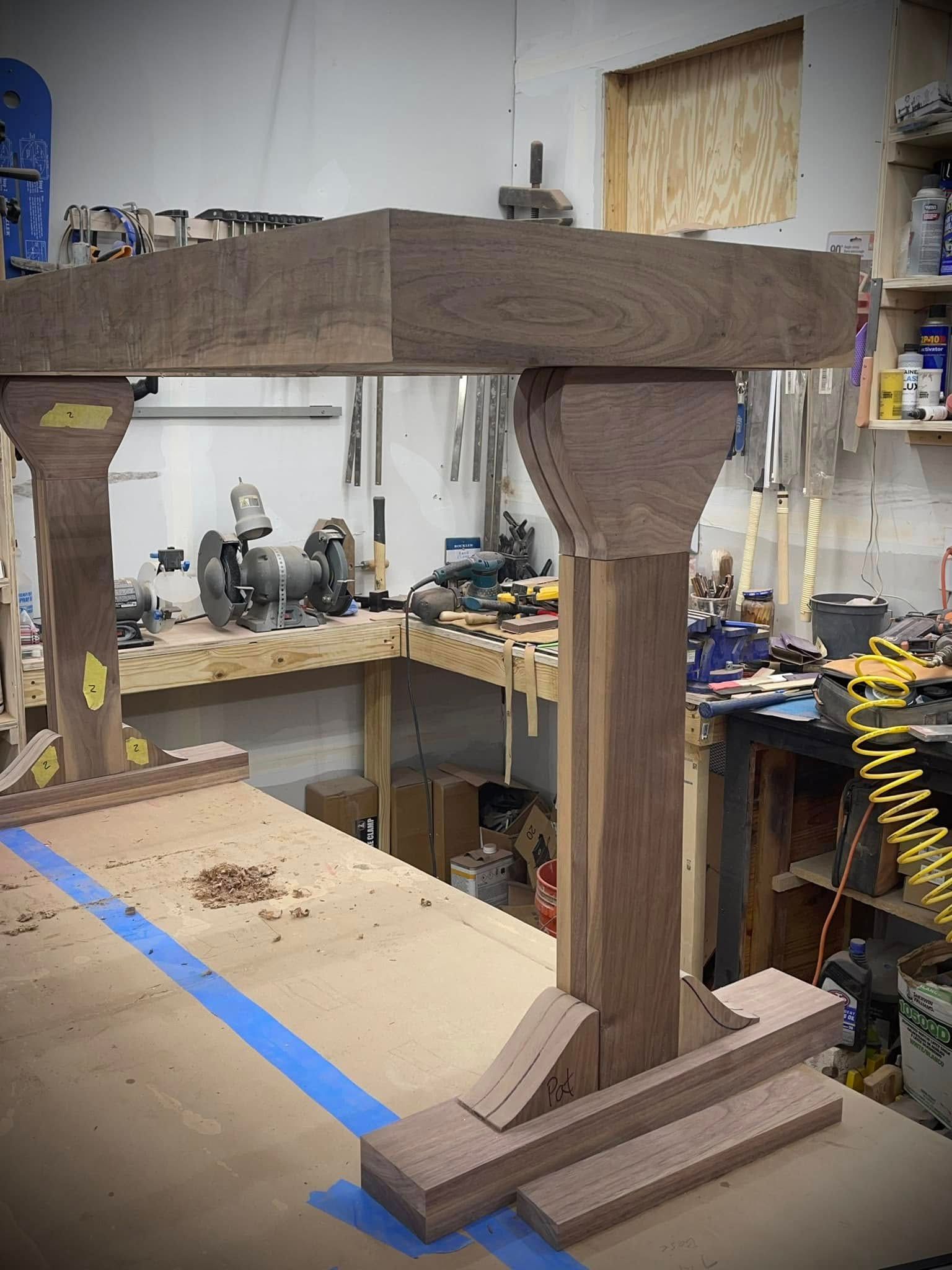 Wood table frame construction in a workshop. Brown wood pieces are assembled on a table, various tools in the background.