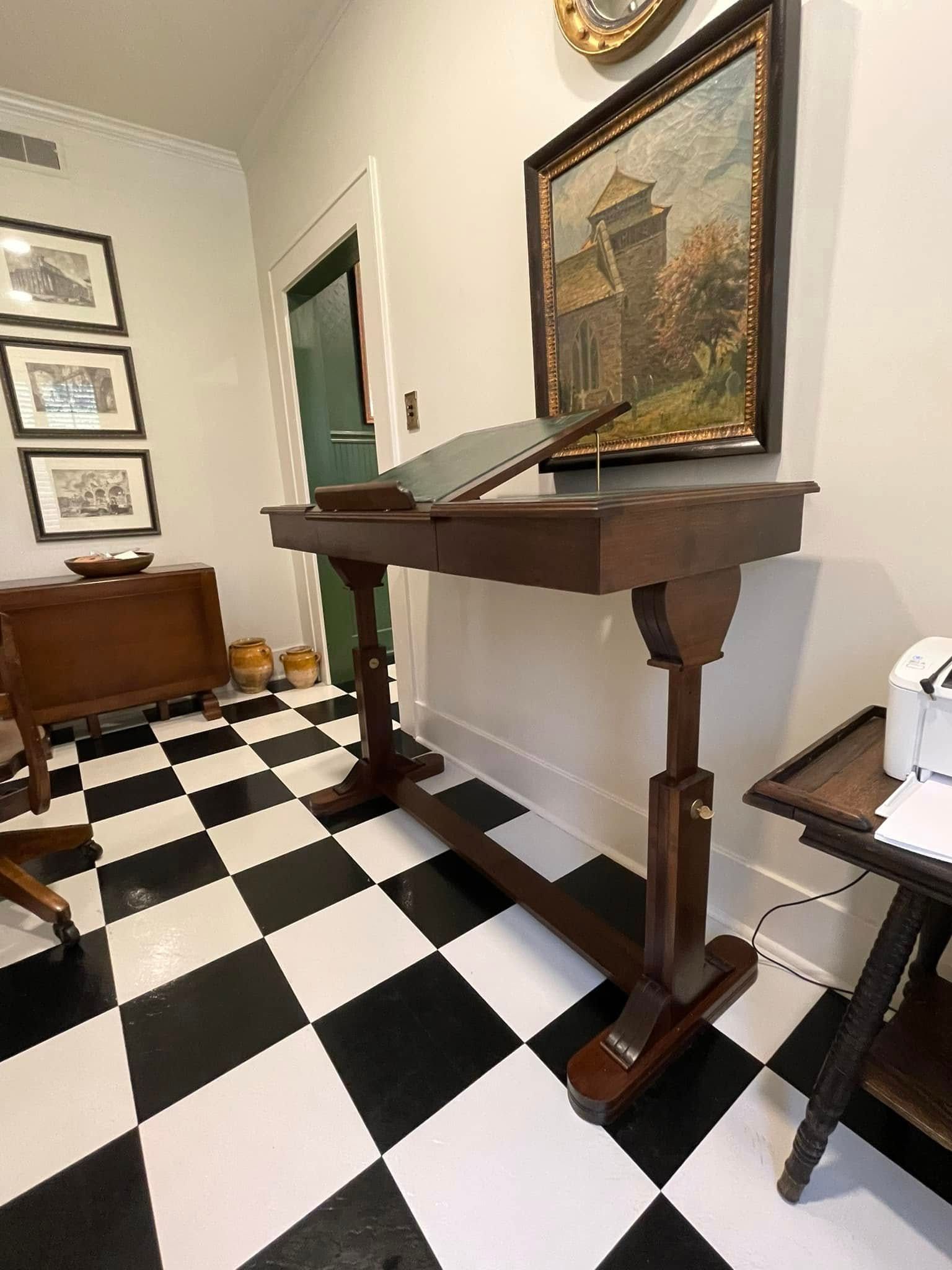 A room with black and white checkered floor, featuring a dark wooden lectern and framed artwork.