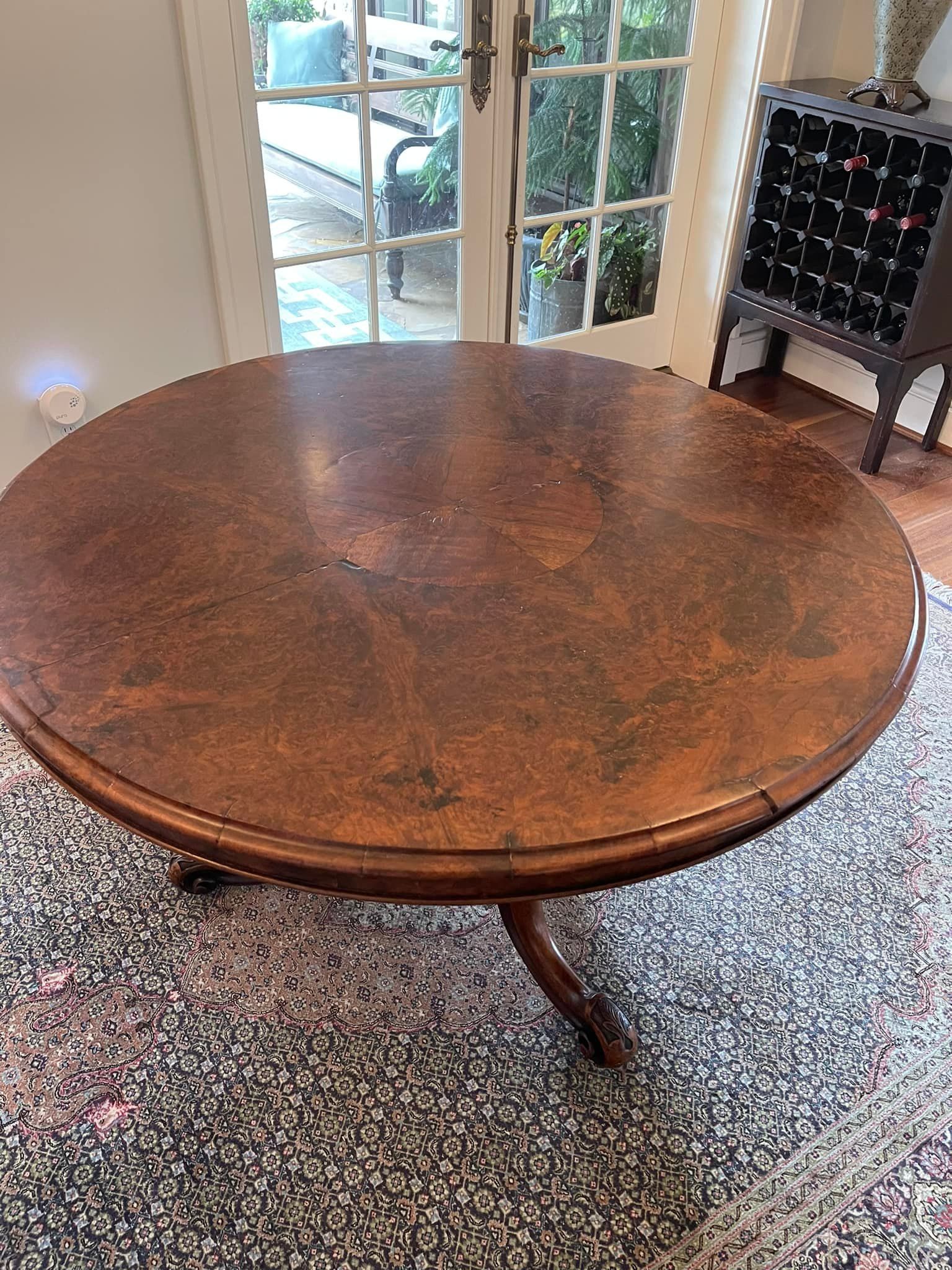 Round, dark wooden table on a patterned rug; French doors and a wine rack are in the background.
