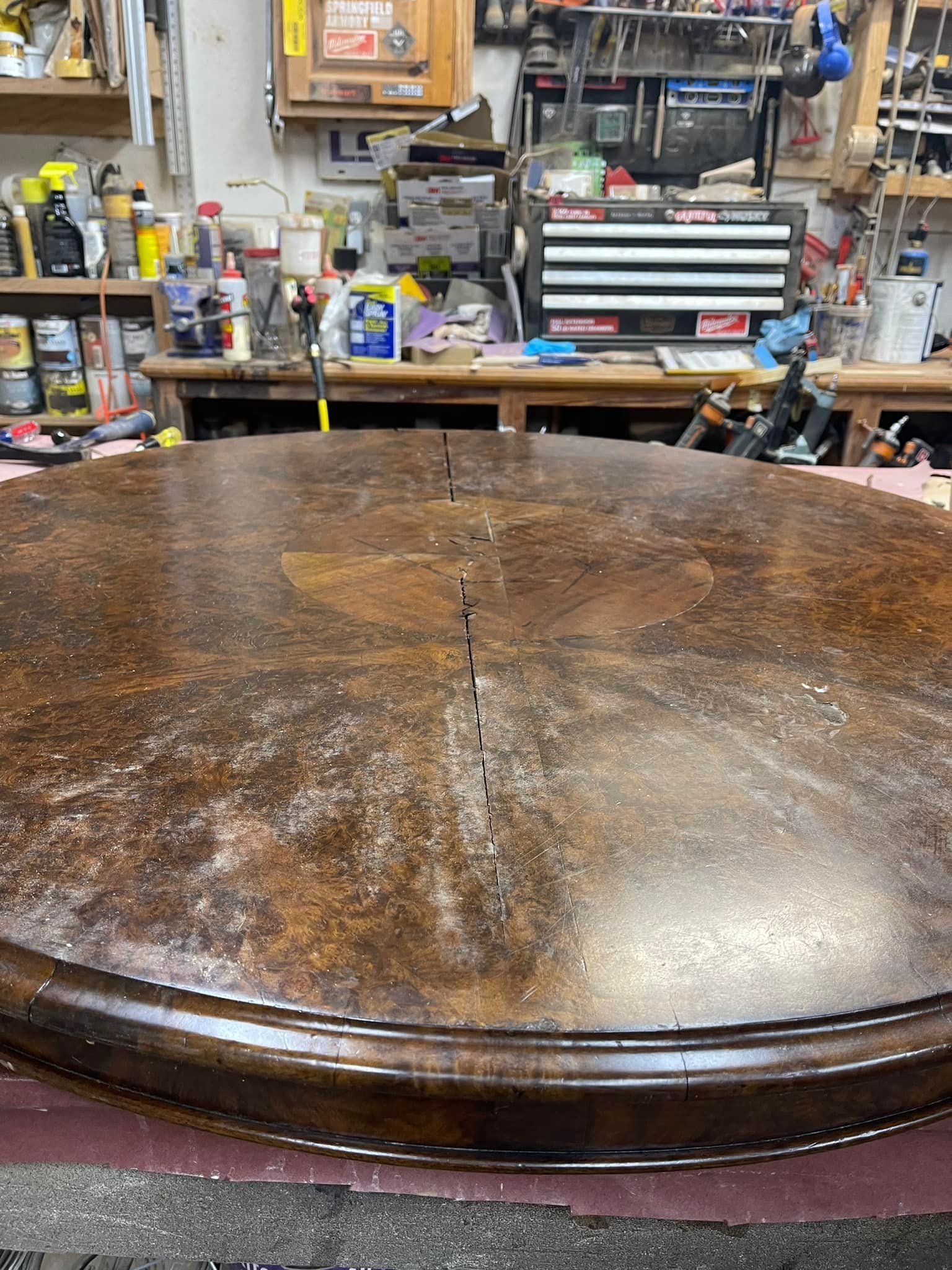Large round wooden table with visible imperfections in a cluttered workshop.