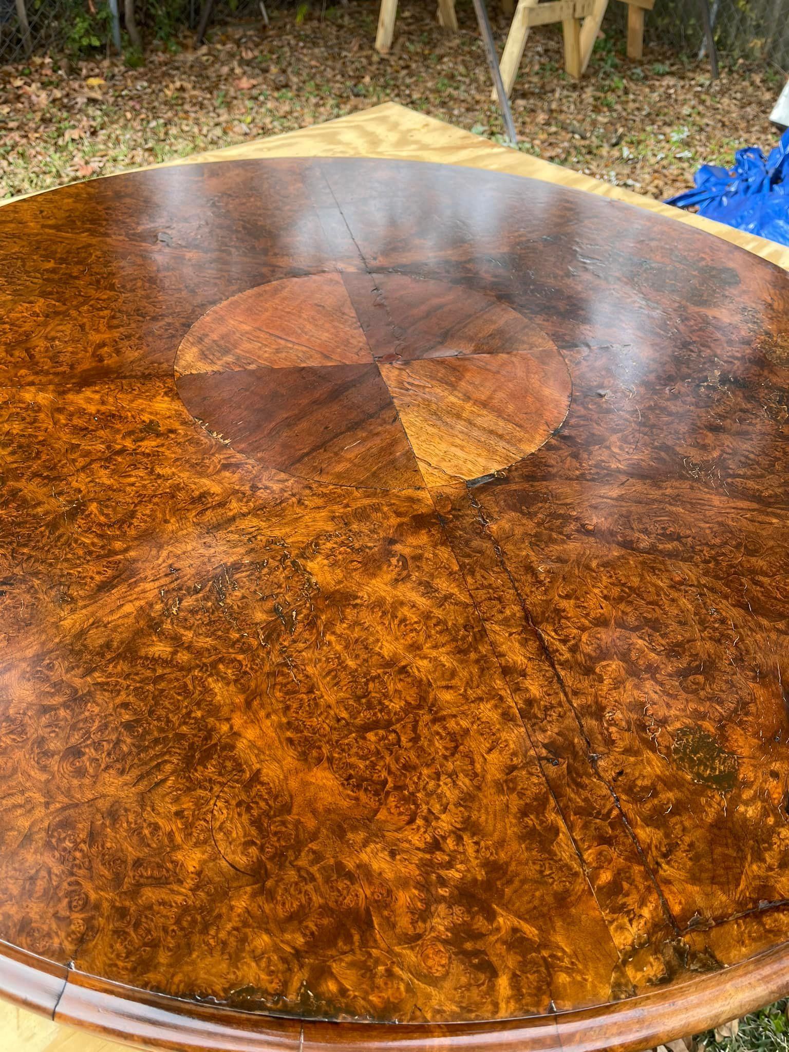 Round wooden table with dark brown, patterned top, outdoors.