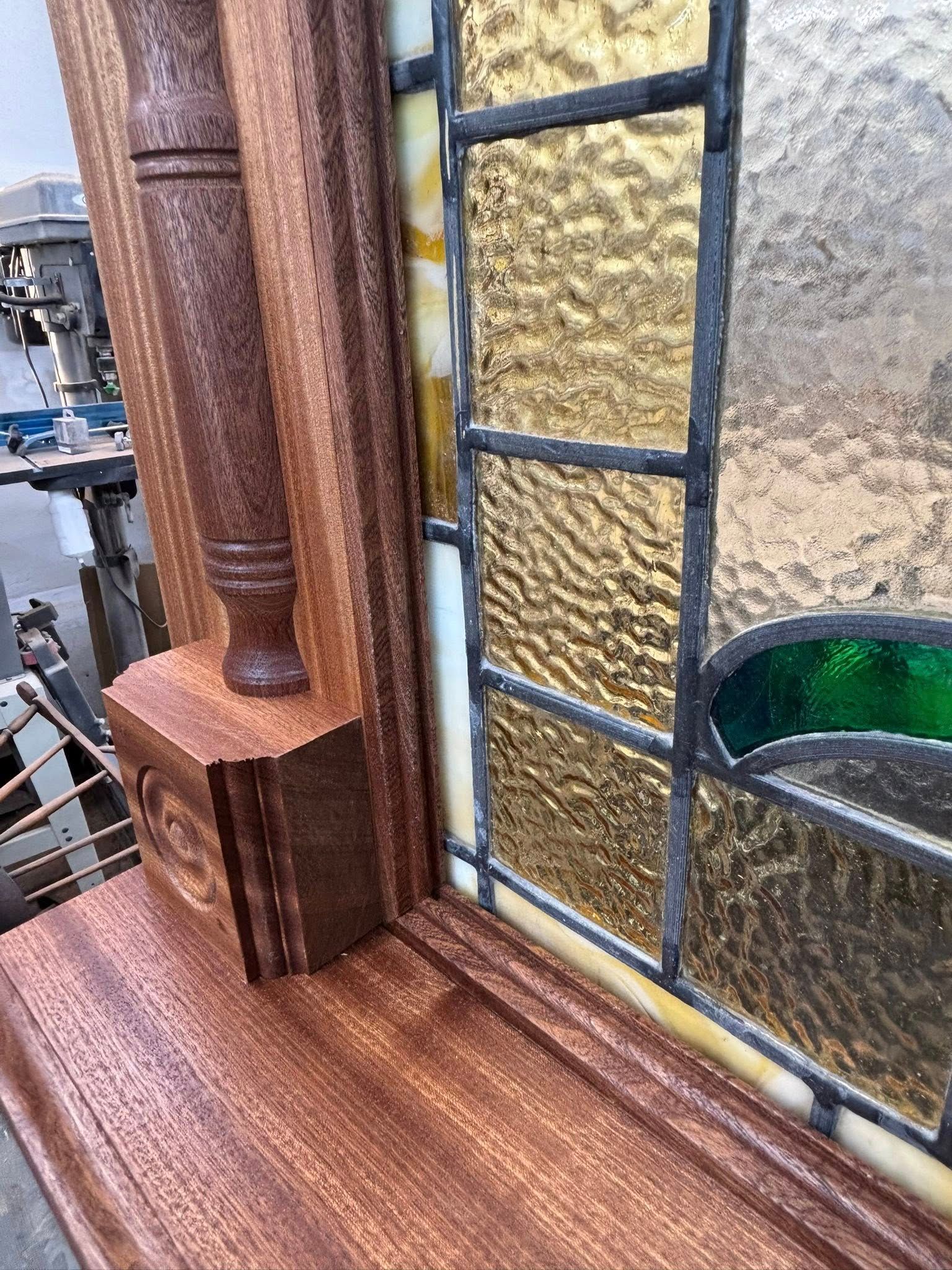 Wooden window frame with stained glass panels; ornate details, gold and green hues.