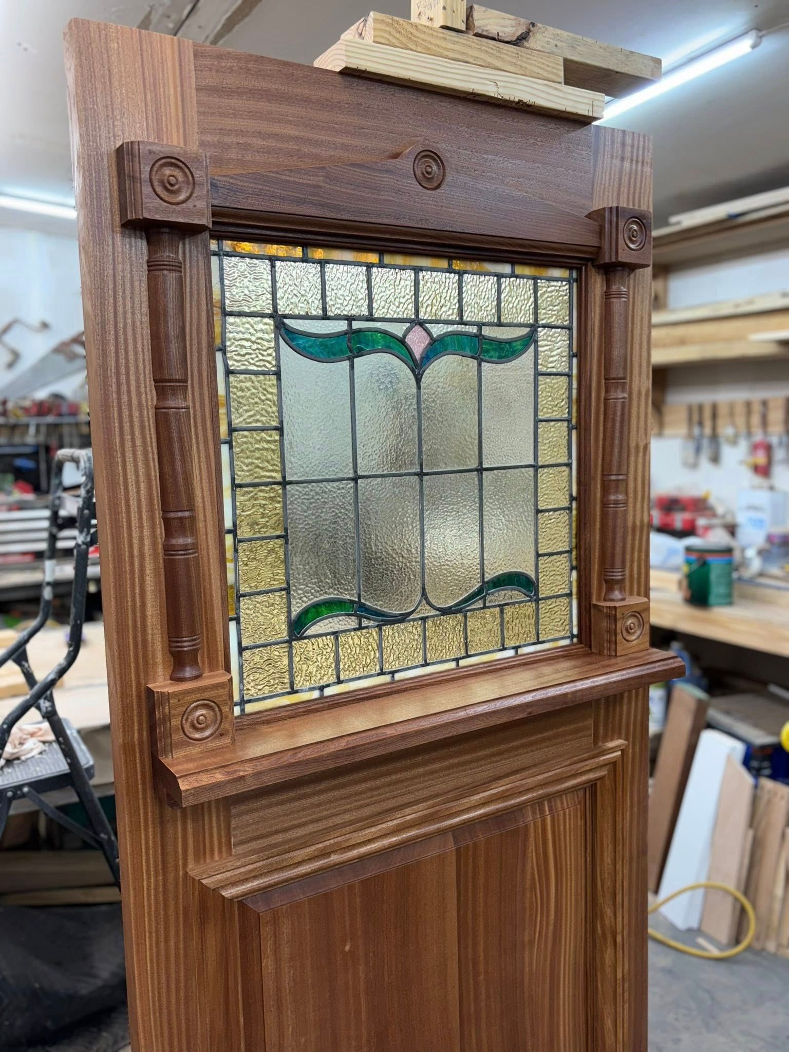 Wooden door with stained glass window, surrounded by decorative trim in a workshop.